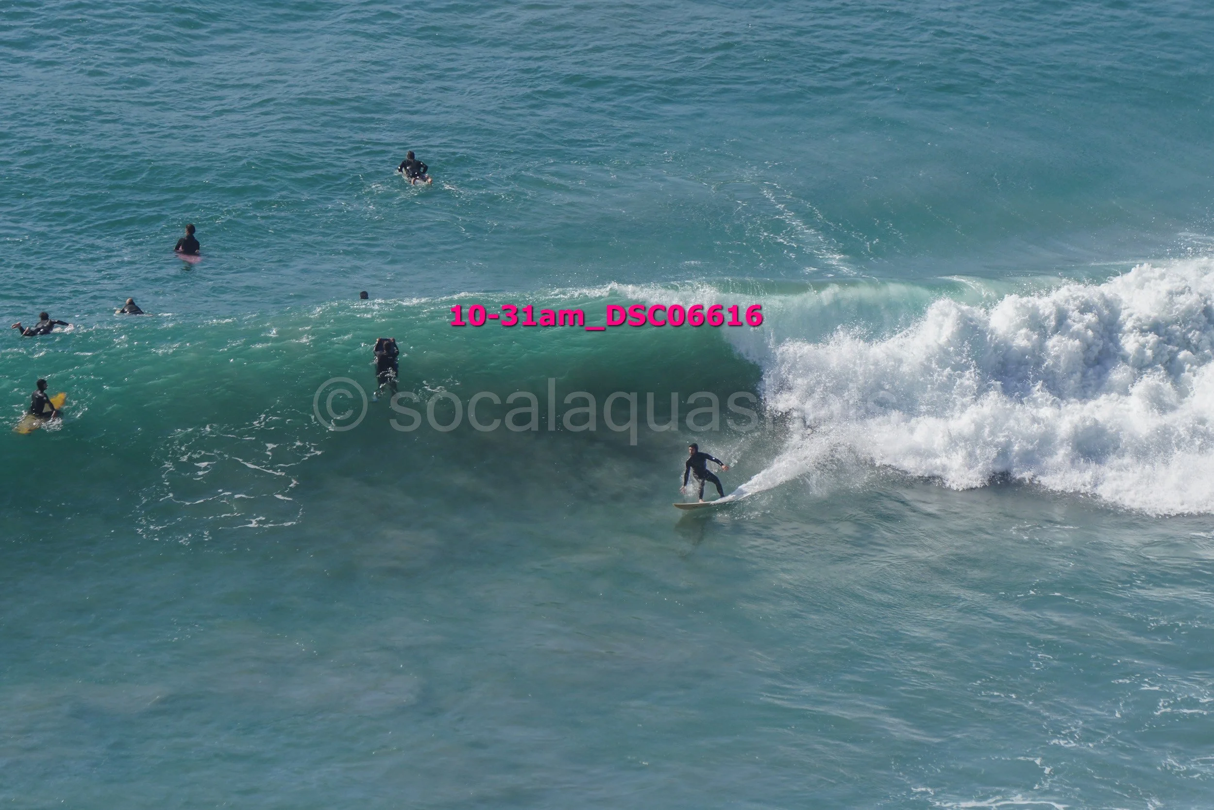 Surfer riding a wave with several people in the water nearby.