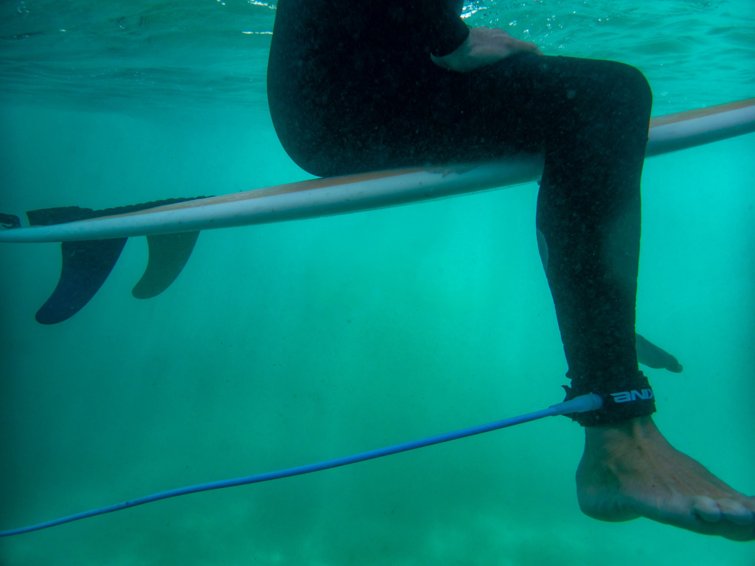 Person sitting on a surfboard in the water, wearing black wetsuit and ankle strap, holding a paddle for paddleboarding.