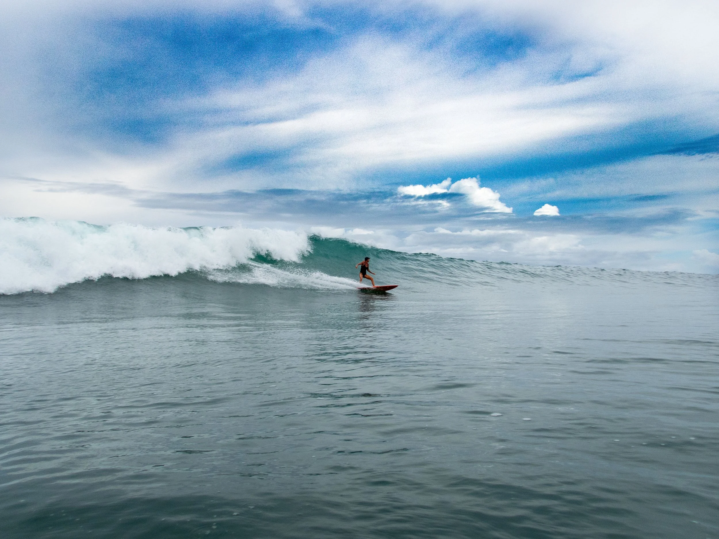 Surfer riding a wave in the ocean under a cloudy sky.