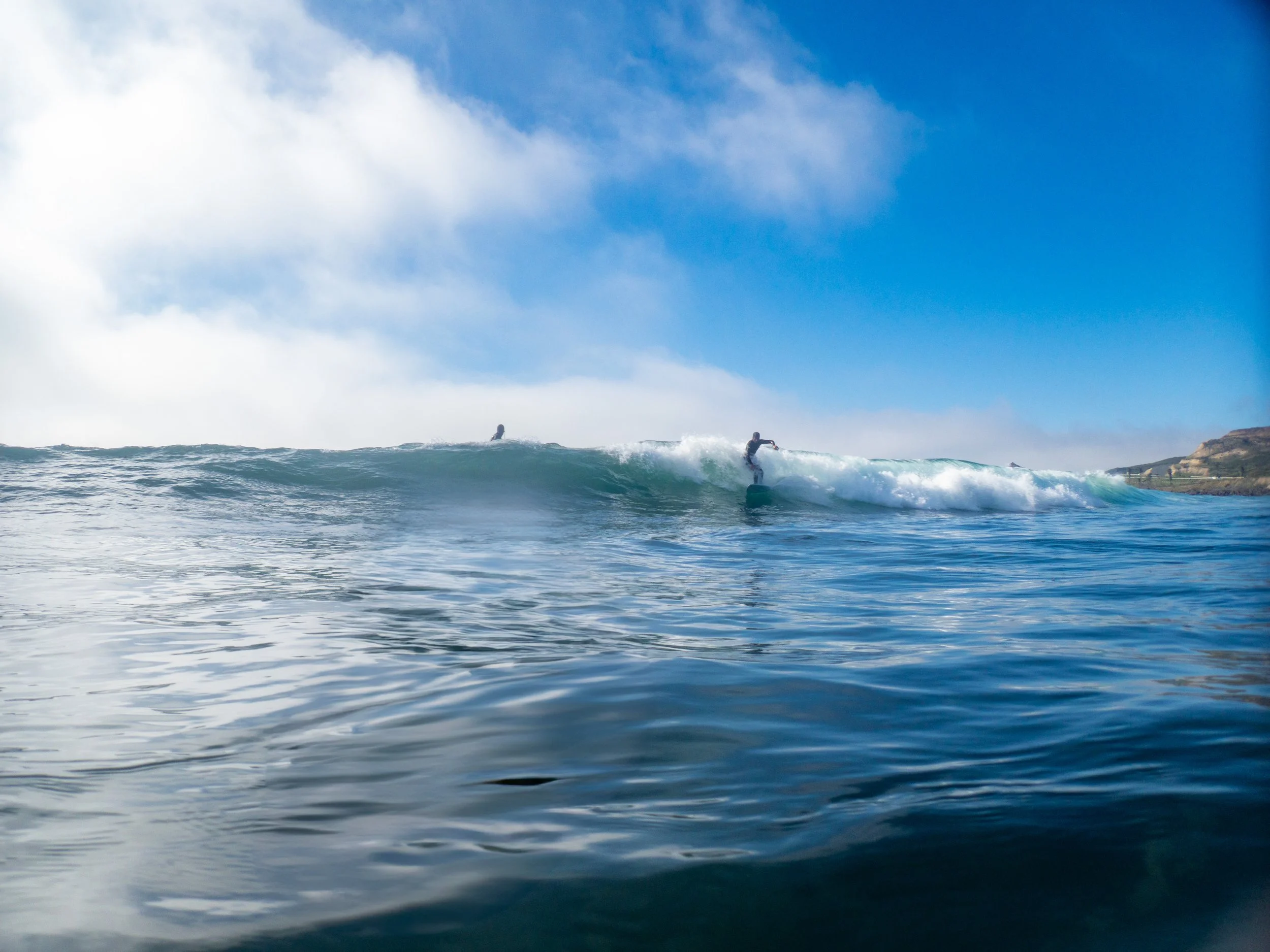 A person surfing on a wave in the ocean with clear blue sky and distant land in the background.