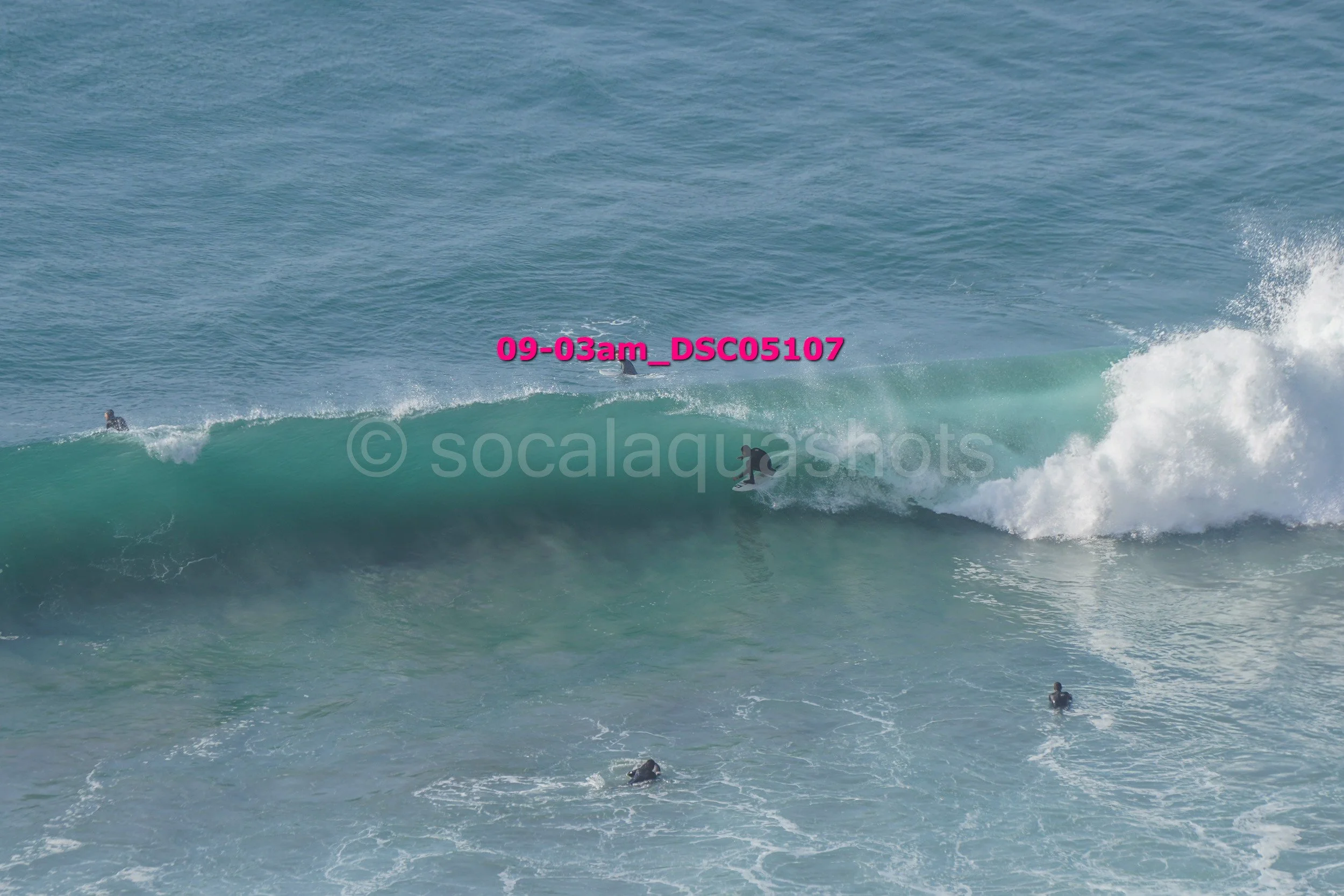 A surfer riding a wave with three other surfers in the water and the ocean in the background.