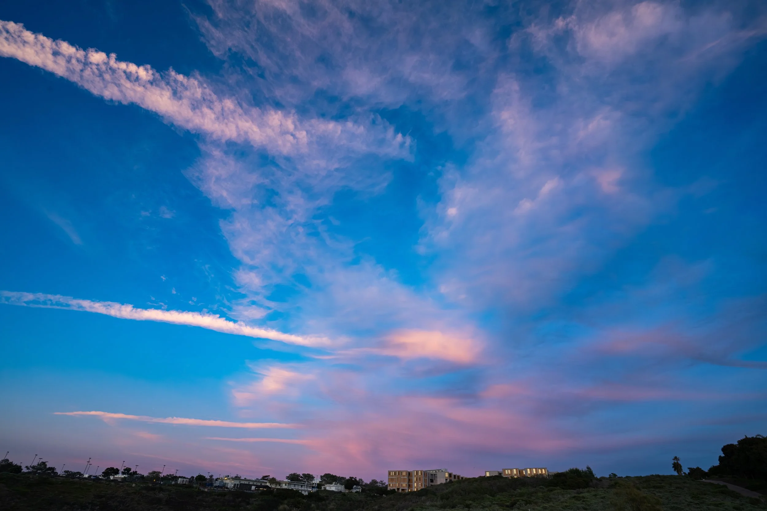 Colorful sunset sky with pink and purple clouds over a residential area with houses and trees.