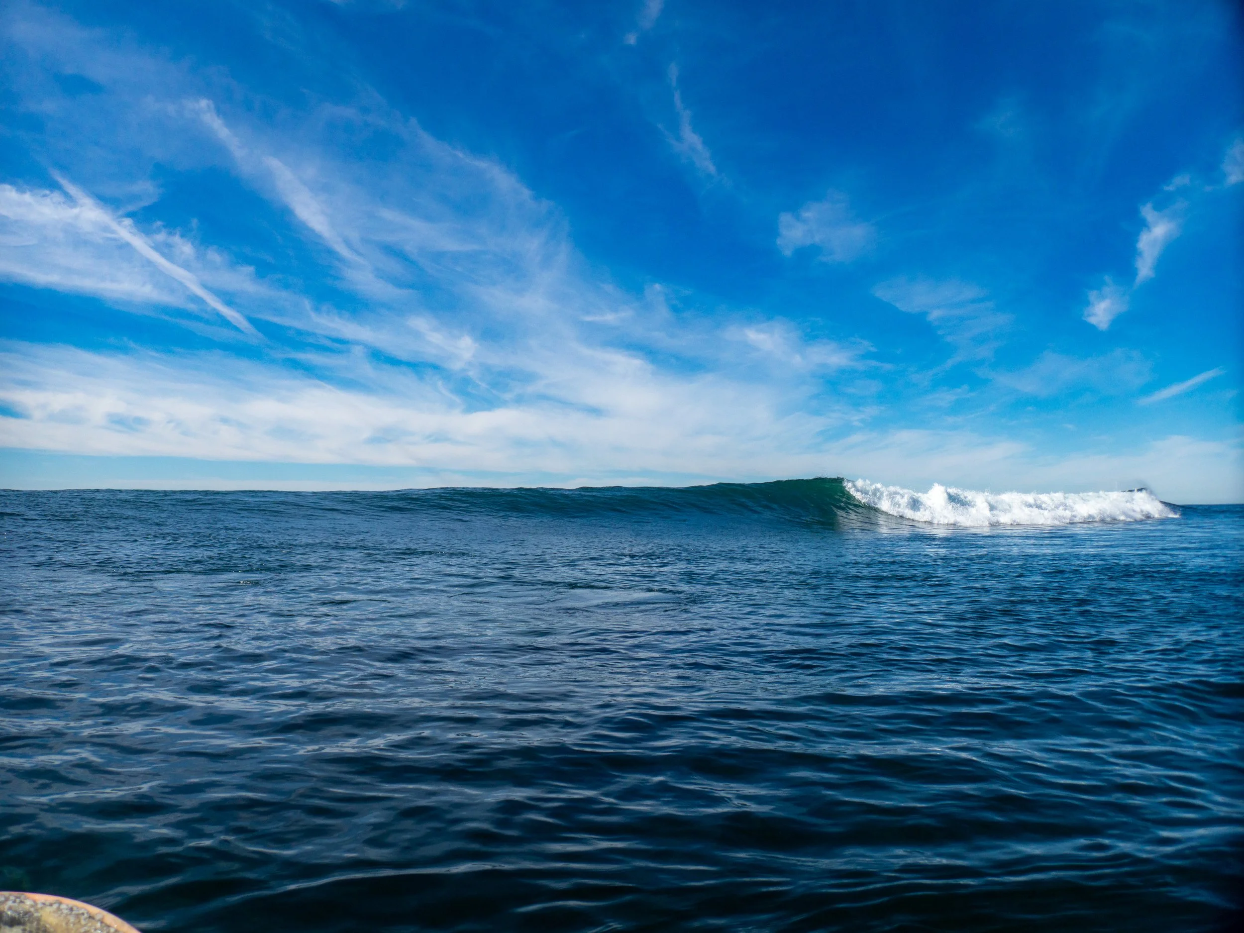 Ocean with a small wave, blue sky with white clouds.