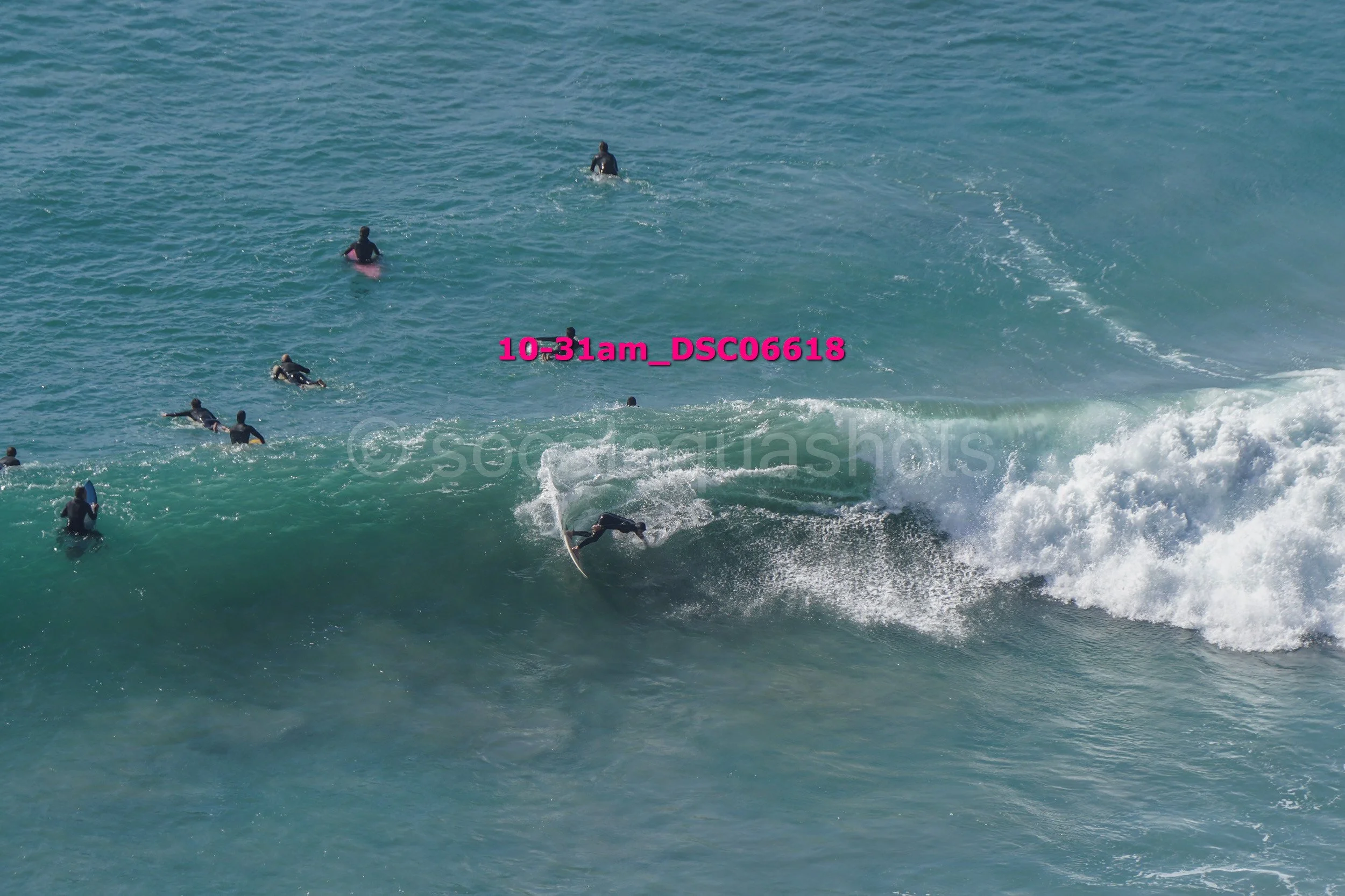 Surfer riding a wave with a group of people in the water watching or waiting nearby.