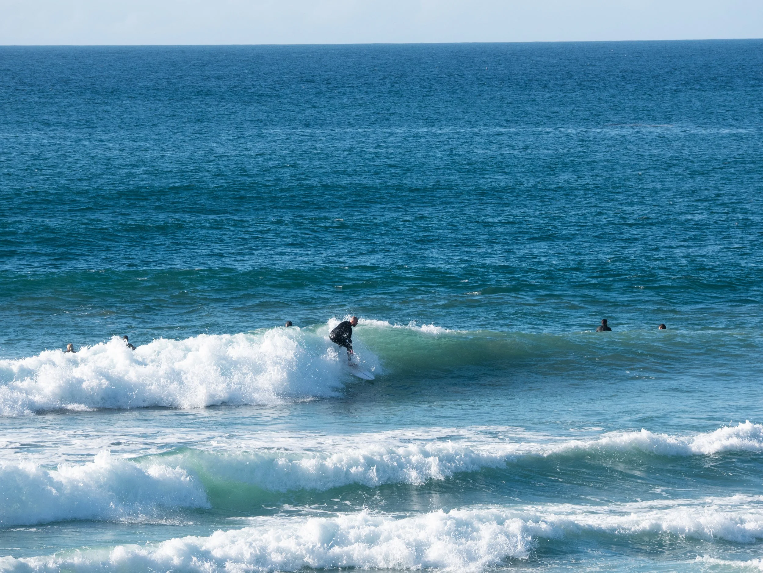 A person surfing on a wave in the ocean with several other people in the water nearby.