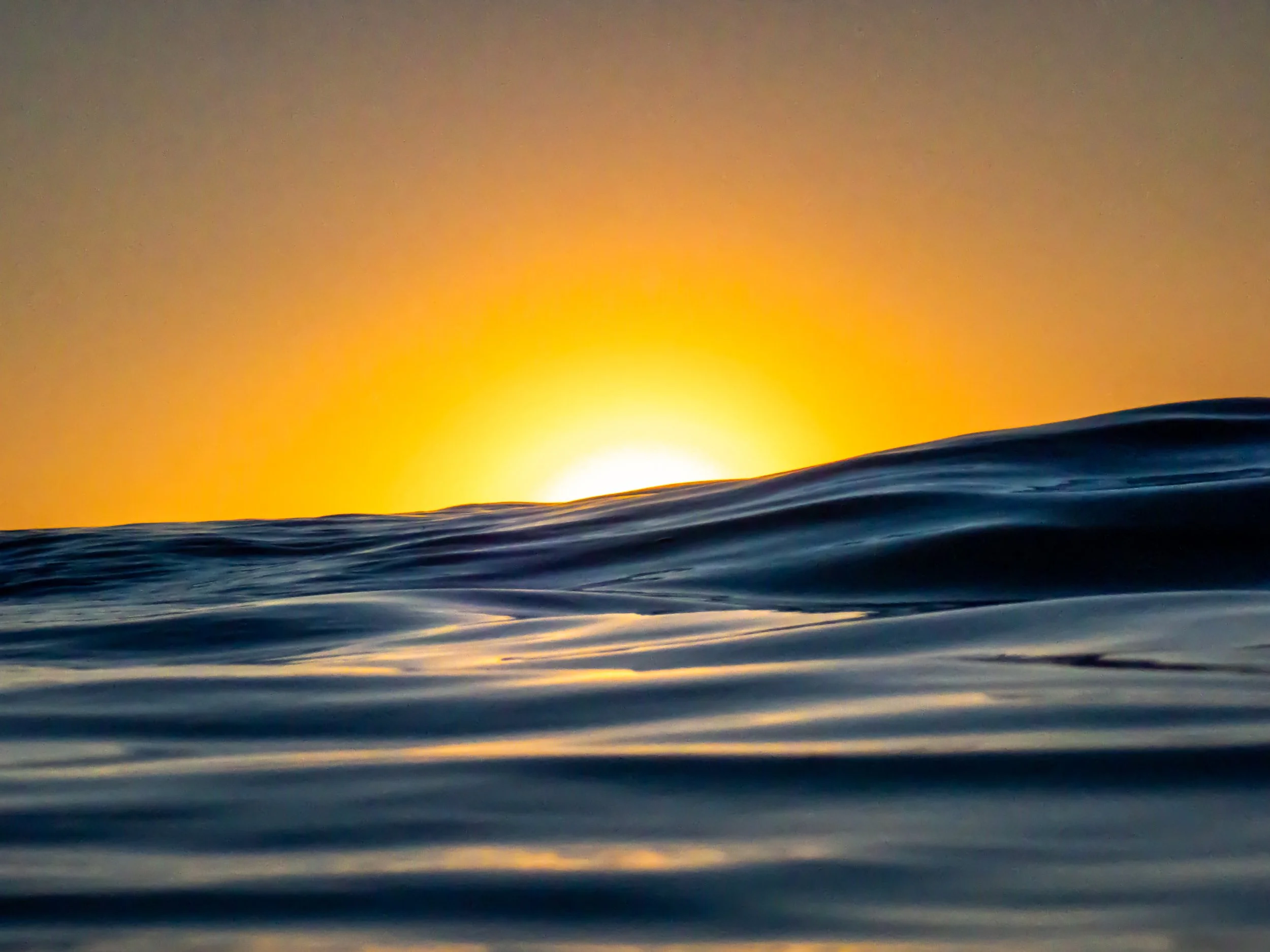 Sunset over ocean waves with orange sky in the background.