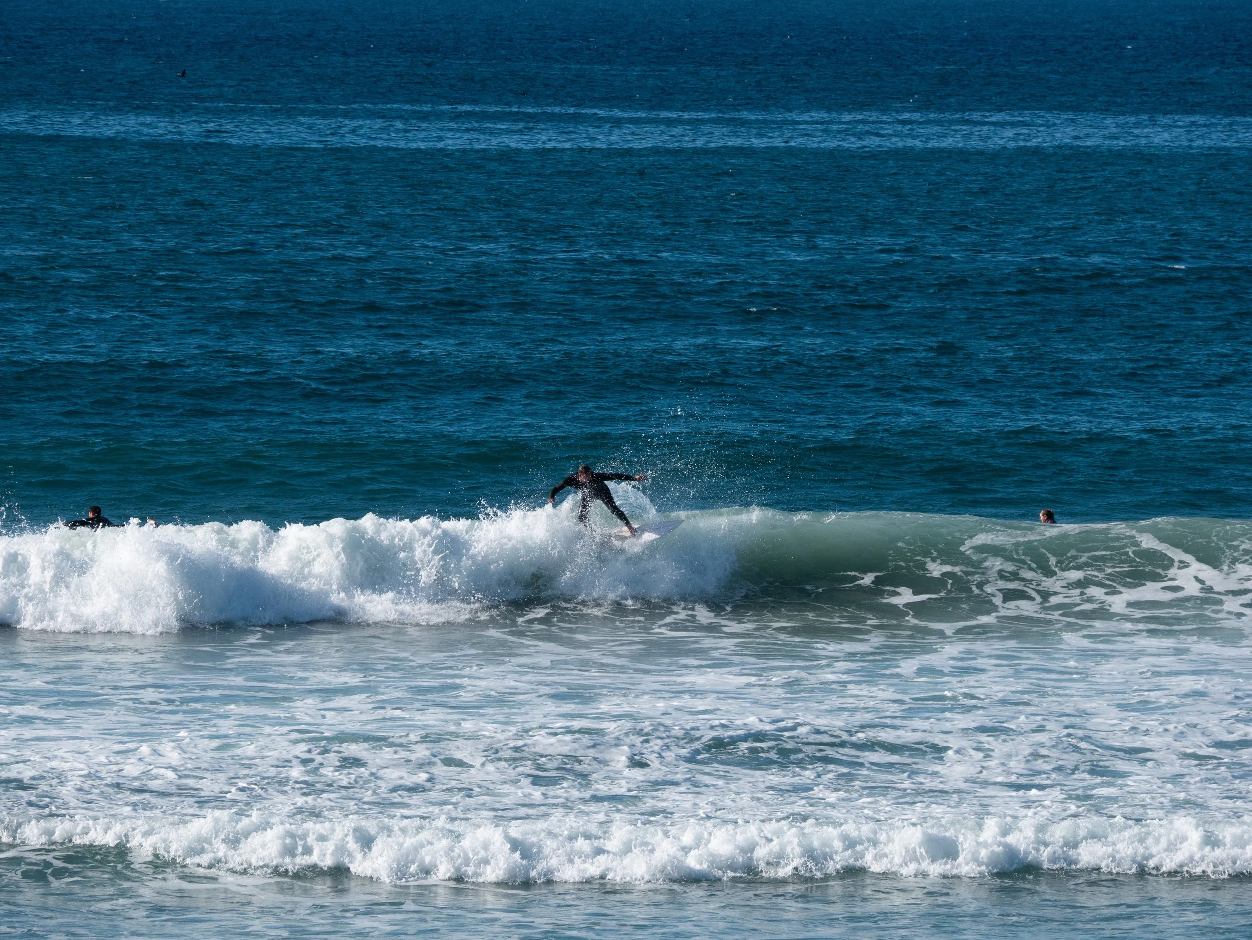 A person surfing on a wave at the beach, with two other people in the water nearby.