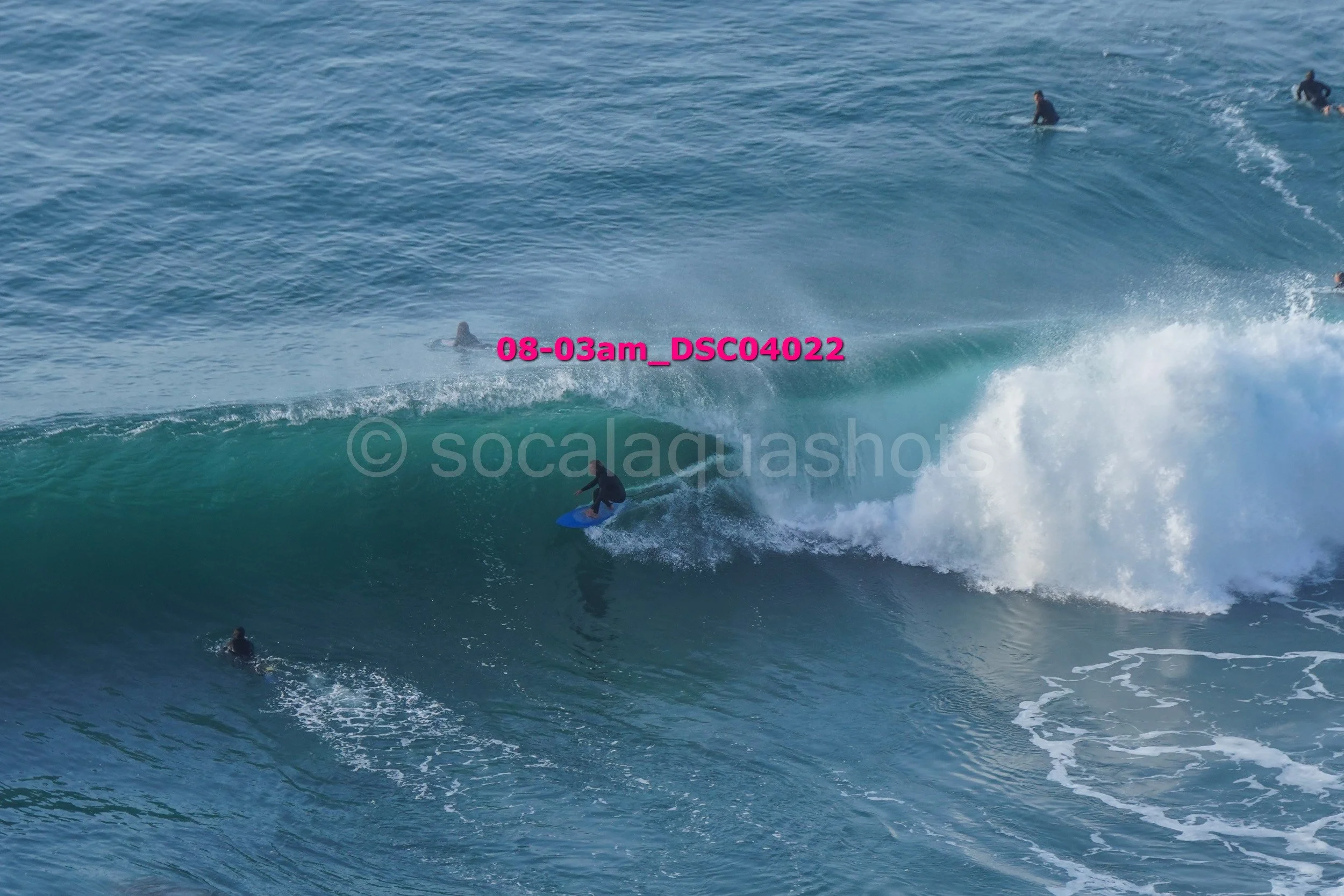 A group of people surfing on large ocean waves, with some paddling and others riding the waves.
