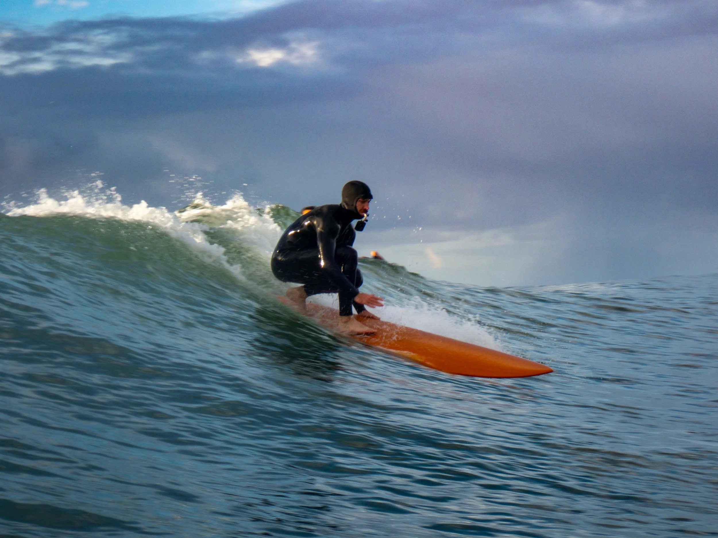 A person wearing a wetsuit surfing on an orange surfboard on the ocean during daytime.