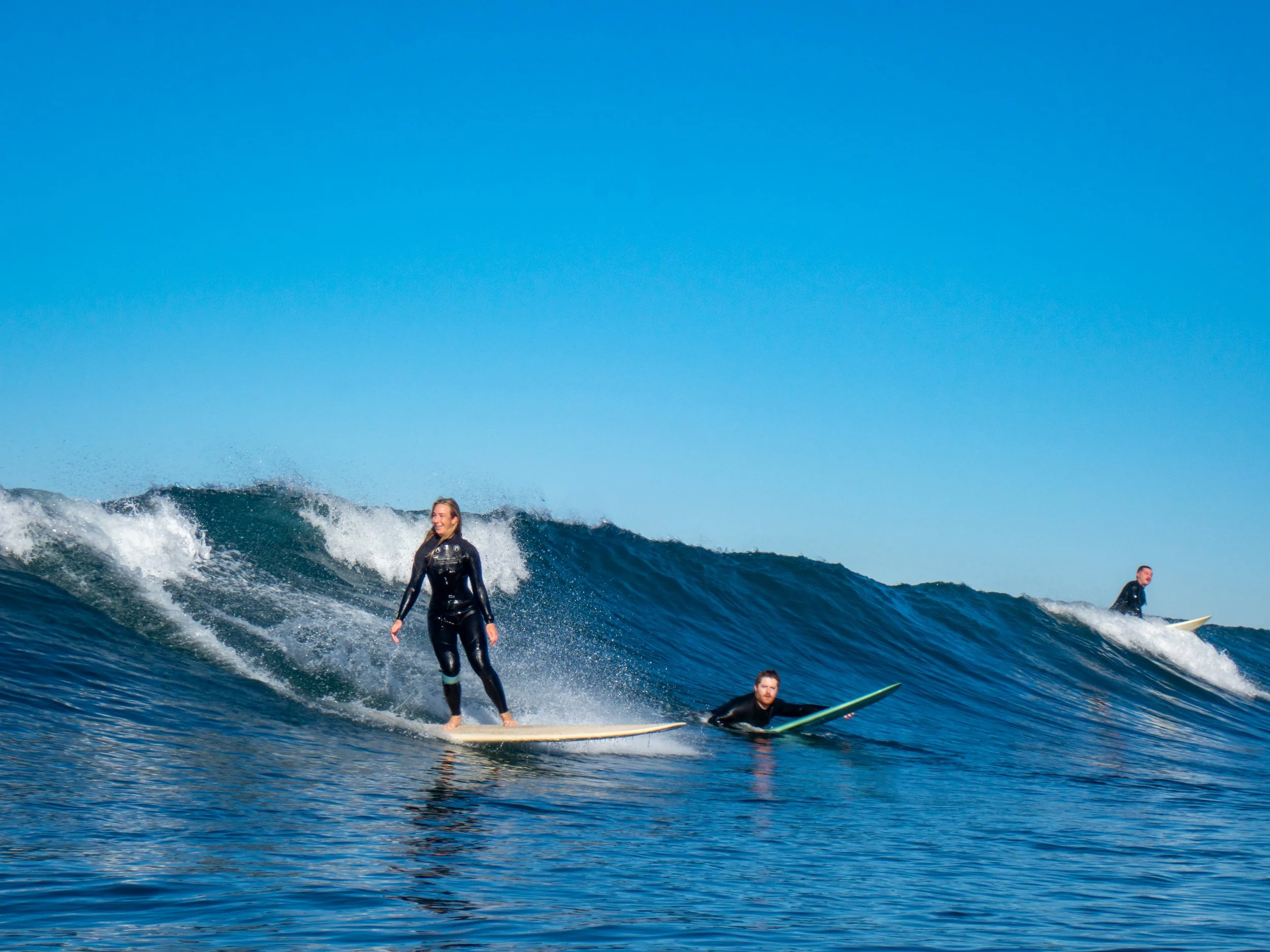 People surfing on ocean waves under a clear blue sky.