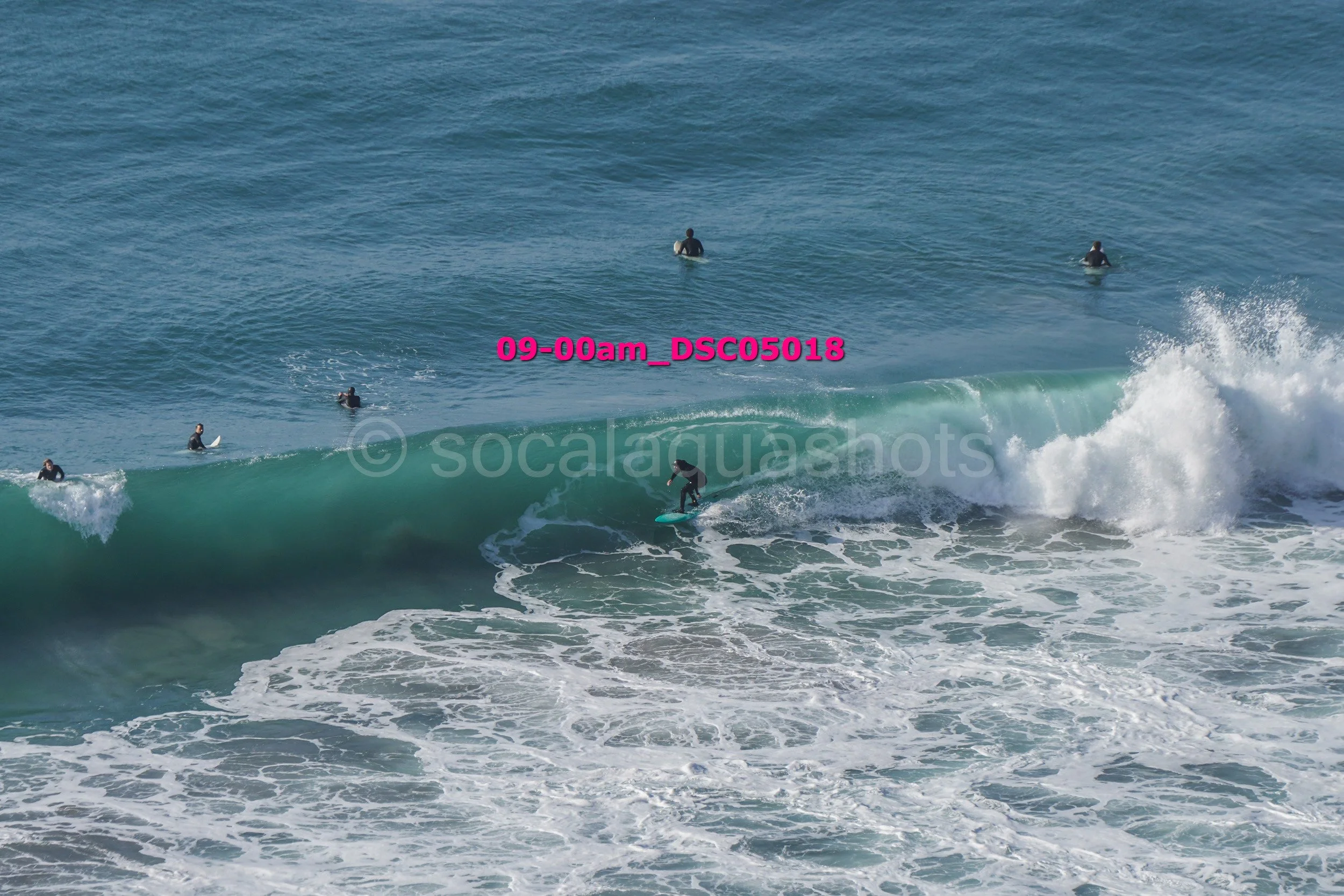 Surfer riding a wave with five surfers in the water in the background.