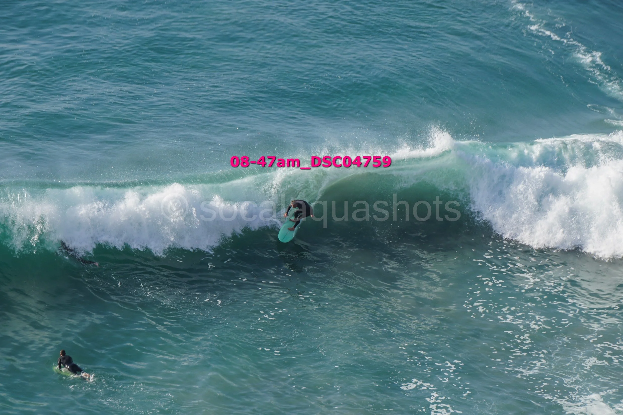Surfer riding a wave in the ocean, another surfer paddling nearby