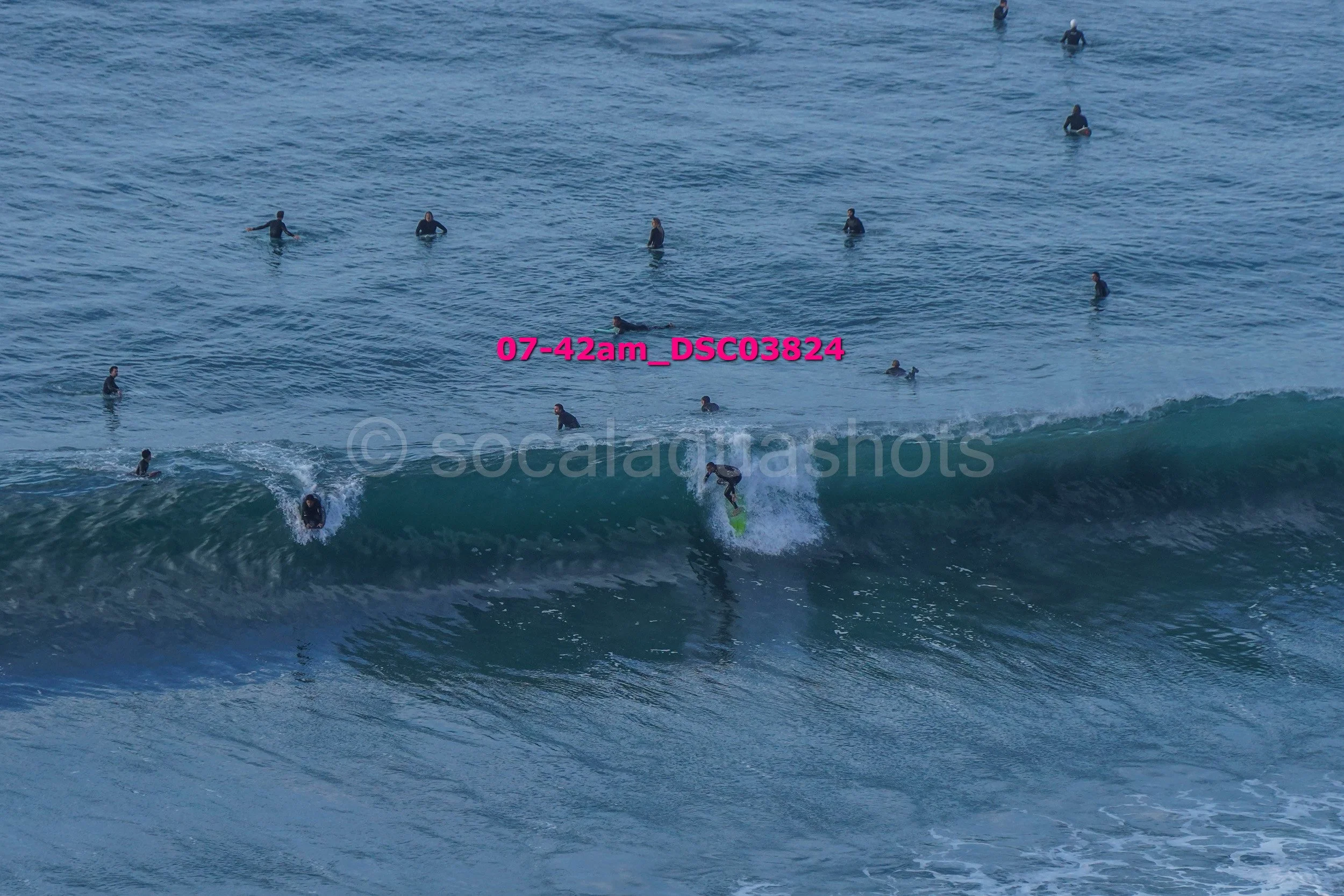 A person riding a wave on a surfboard in the ocean surrounded by many other people in the water.