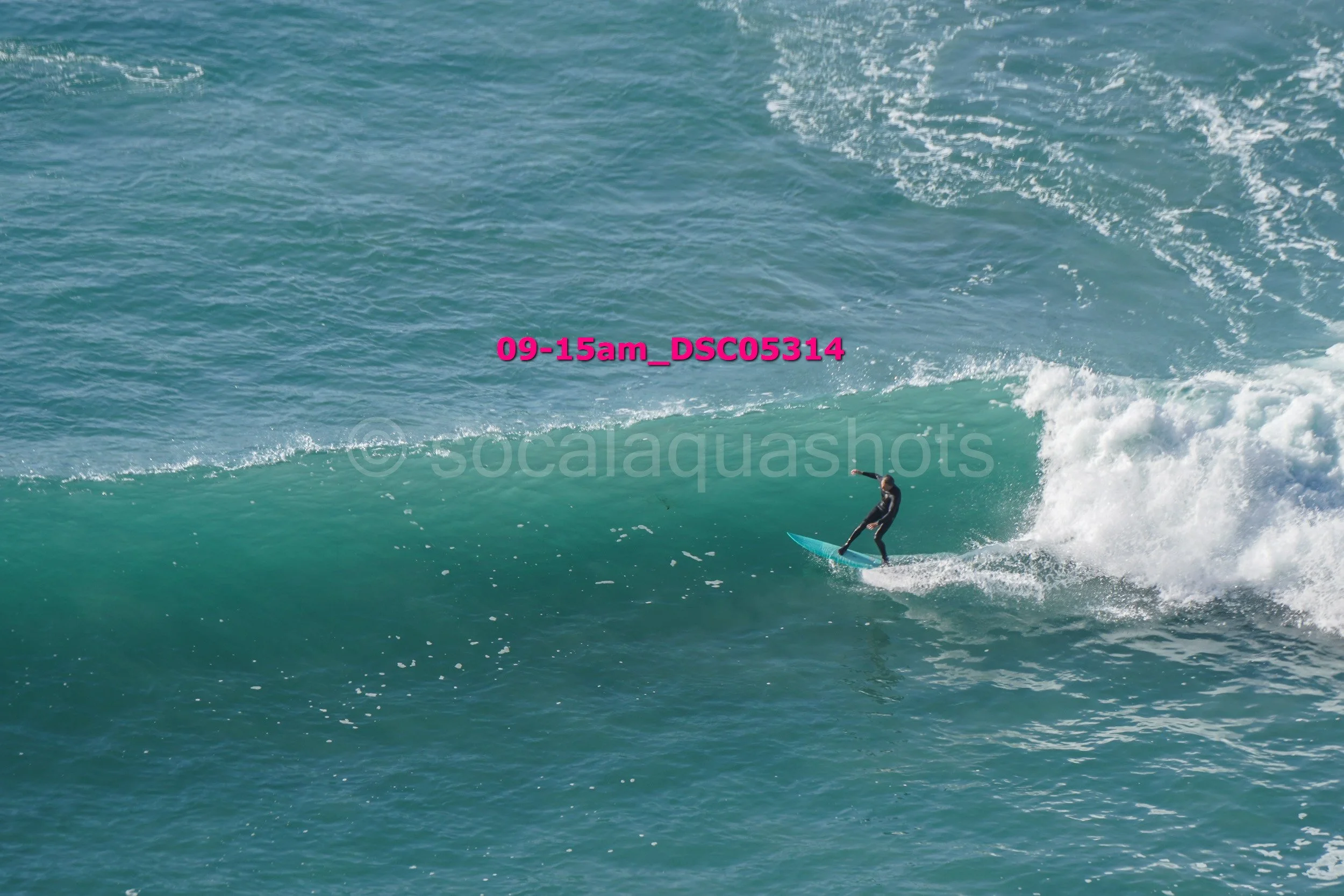 Person in a wetsuit riding a surfboard on a large ocean wave.