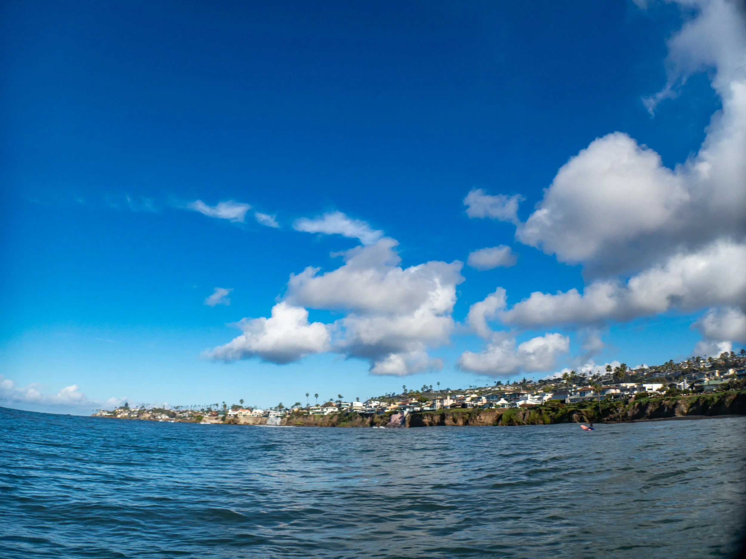 Ocean view with blue water, partly cloudy sky, and houses on a hillside.