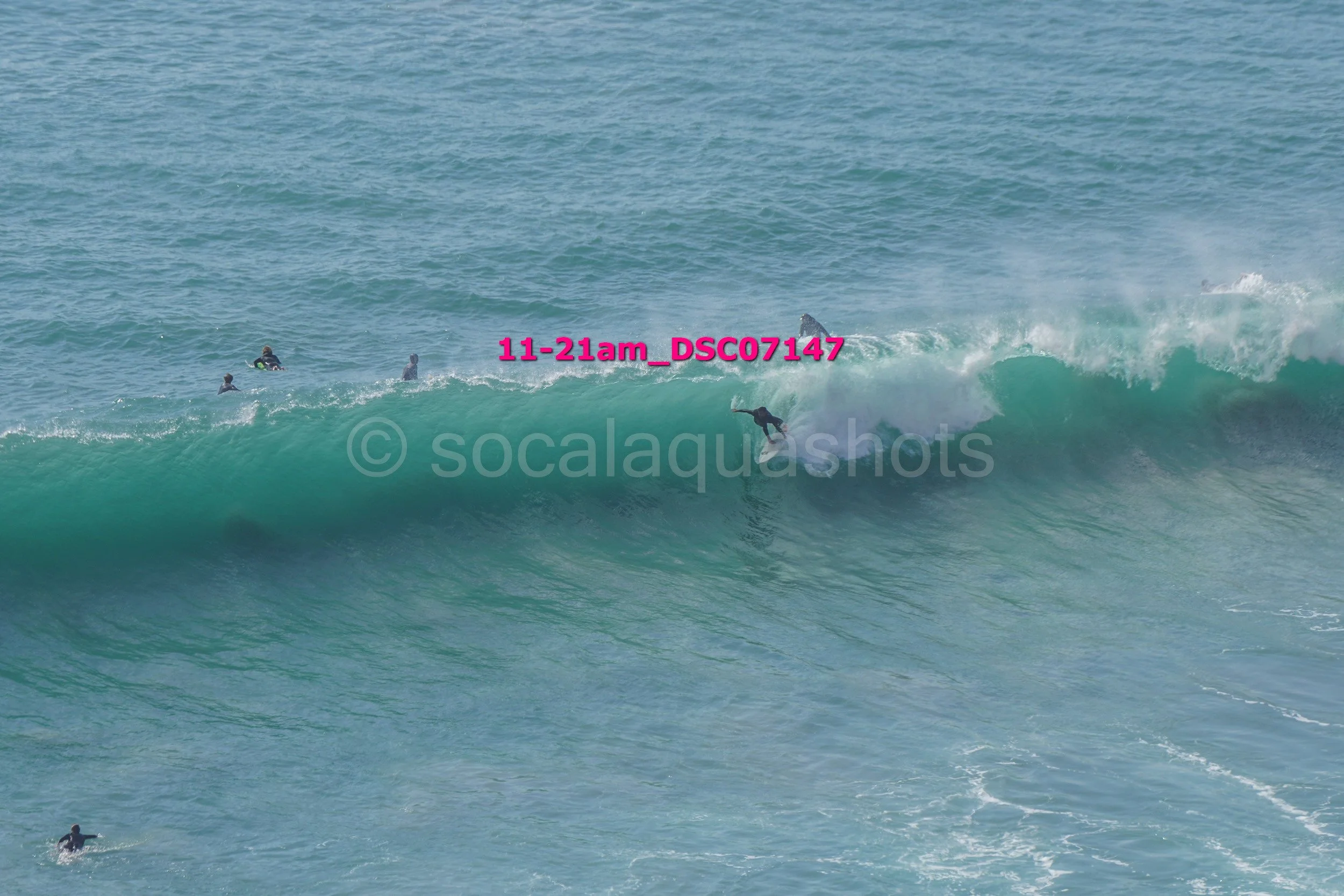 Surfer riding a large wave with several people in the water watching nearby.