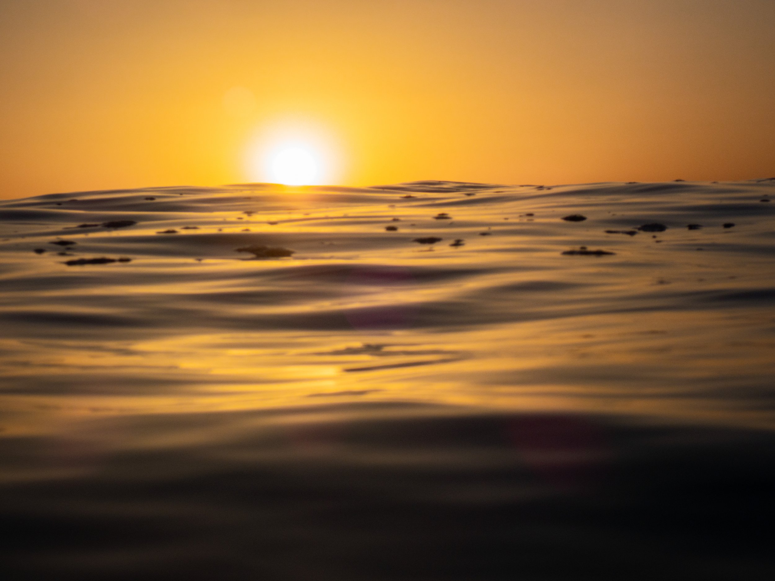 Sunset over the ocean with the sun near the horizon and gentle waves in the foreground.