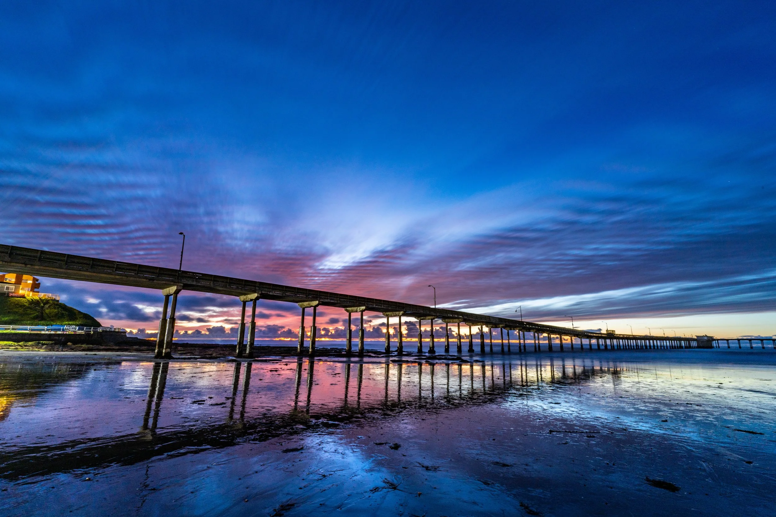 Pier extending into a calm body of water during sunset with colorful sky and clouds