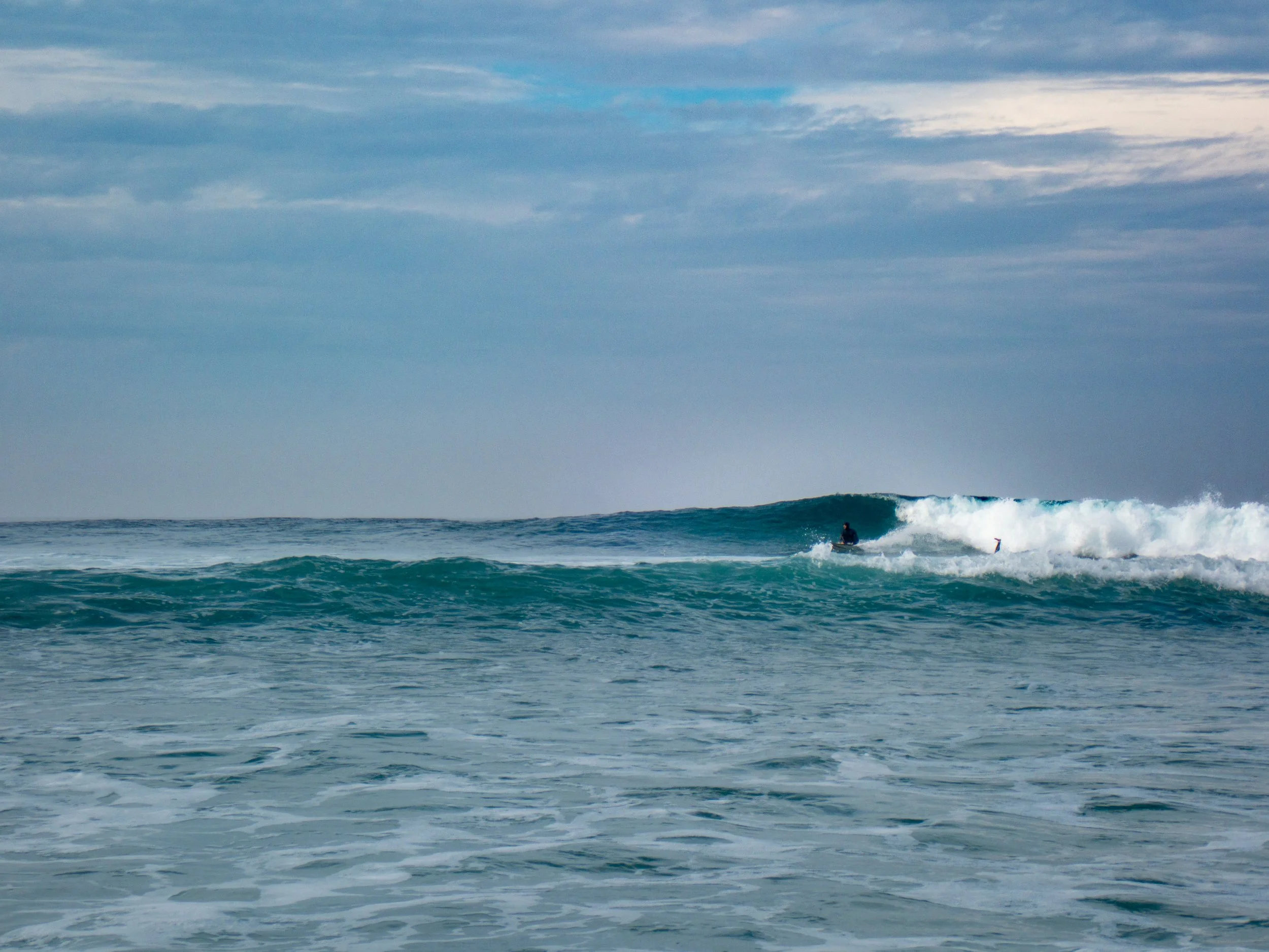 Surfer riding a wave in the ocean under a cloudy sky