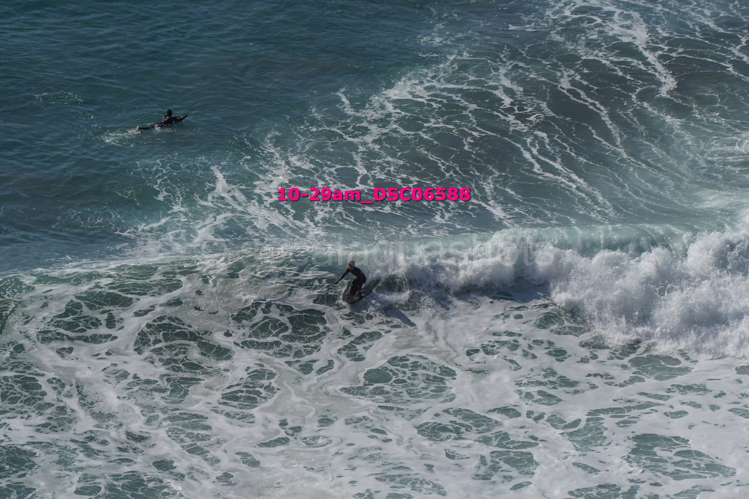 A person surfing on a wave in the ocean with another swimmer seen swimming in the water nearby.