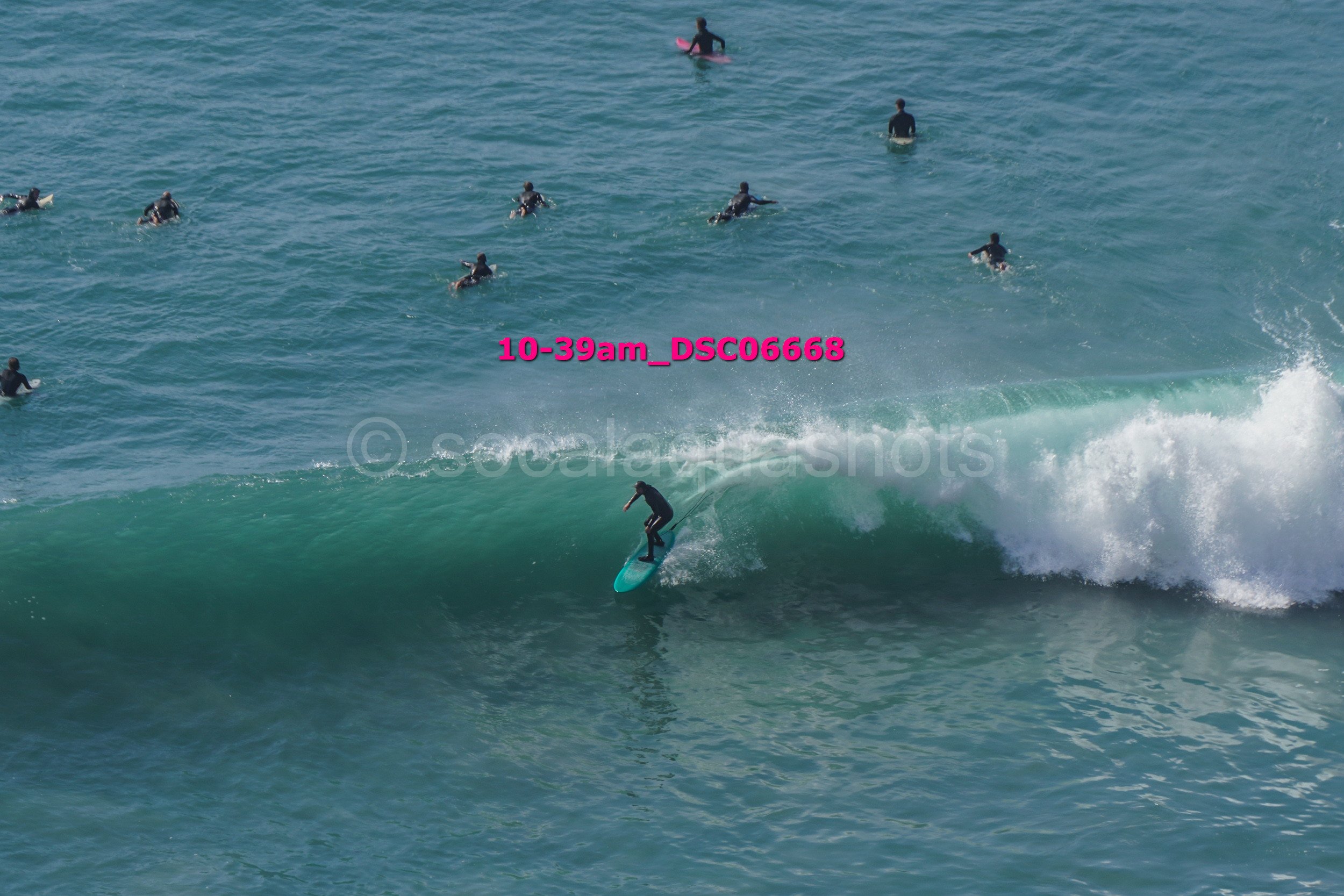 A person surfing on a wave with several people in the background in the water.
