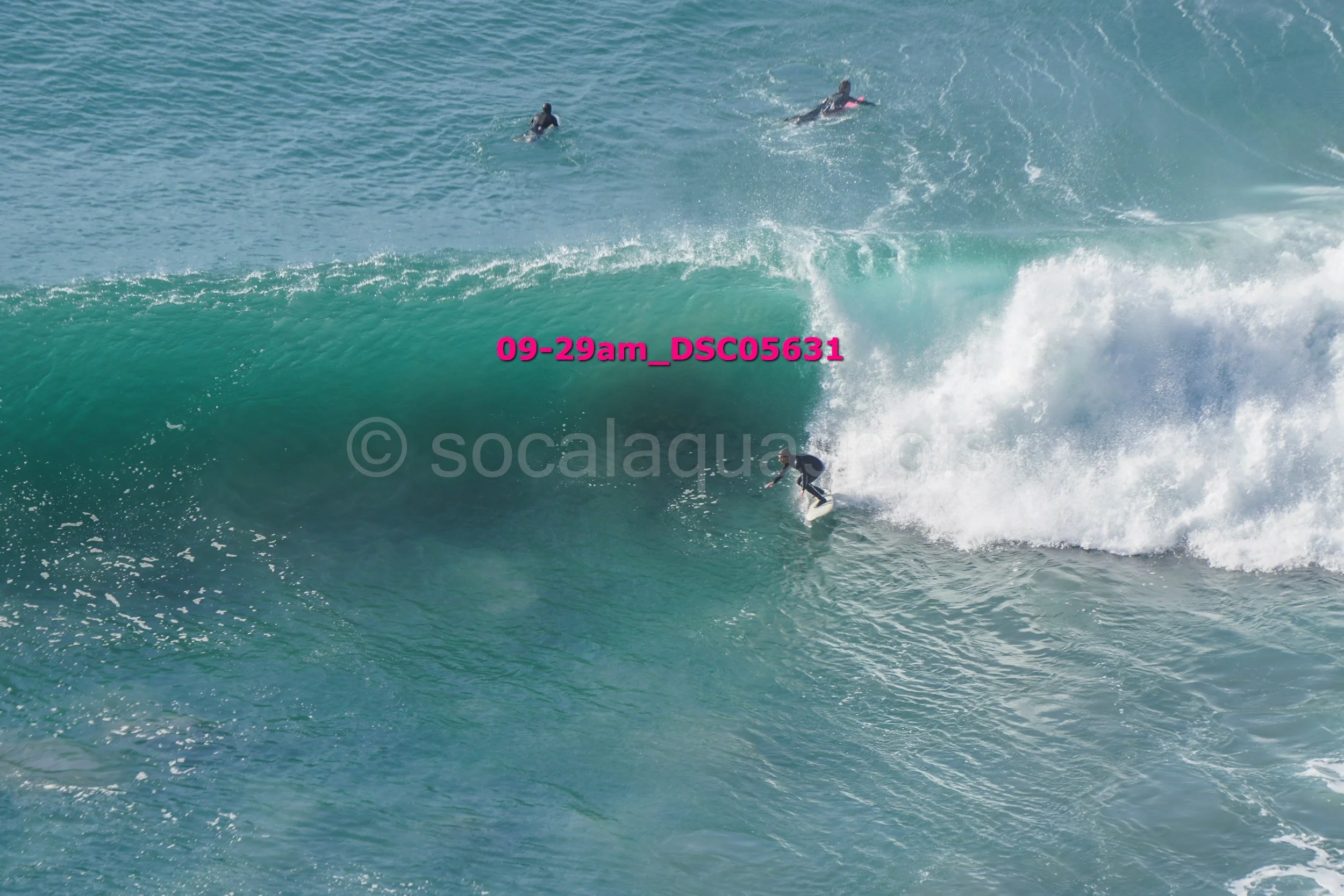 Surfer riding a large wave in the ocean with other surfers in the water in the background.