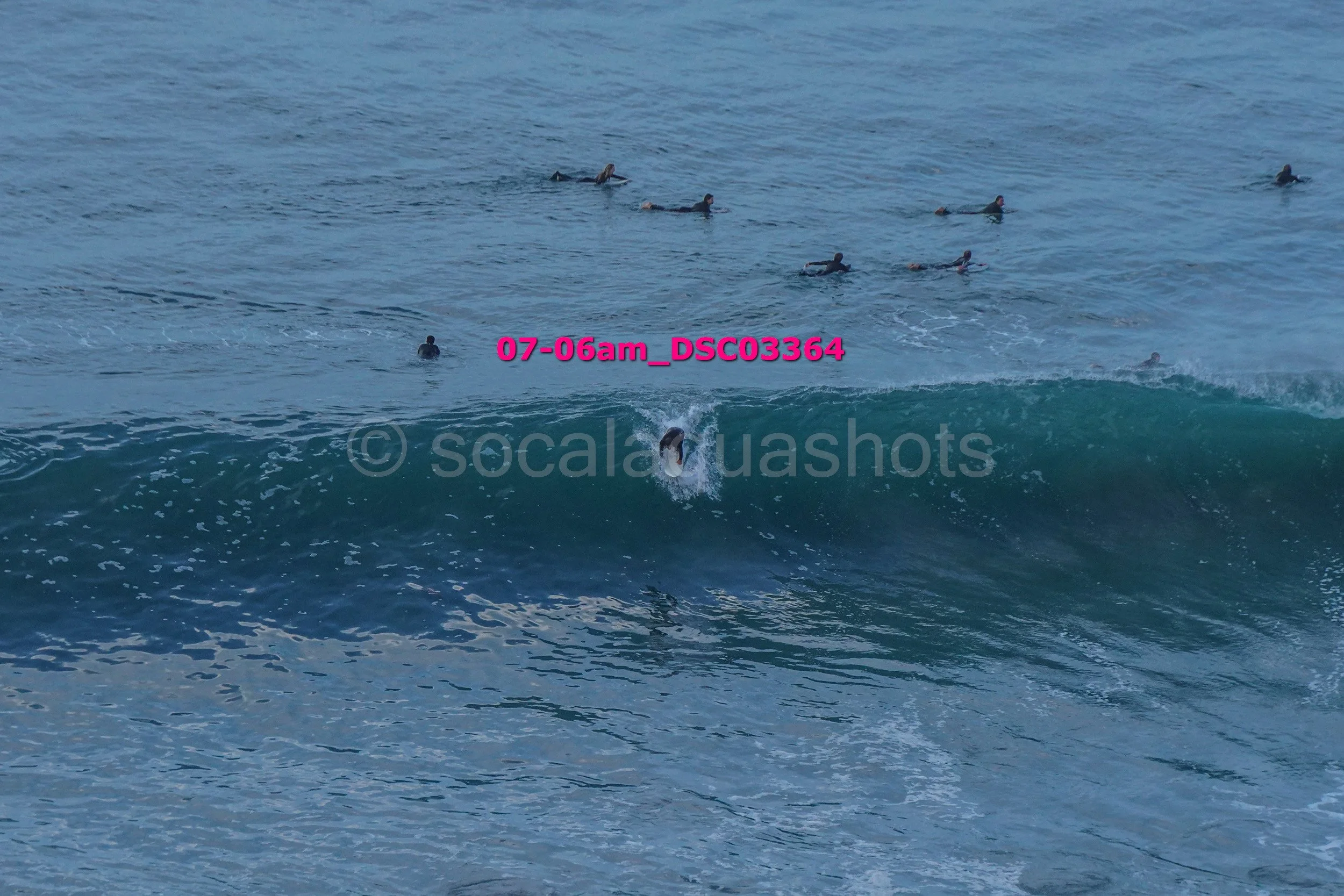 A person surfing a wave with numerous surfers in the background in the ocean.