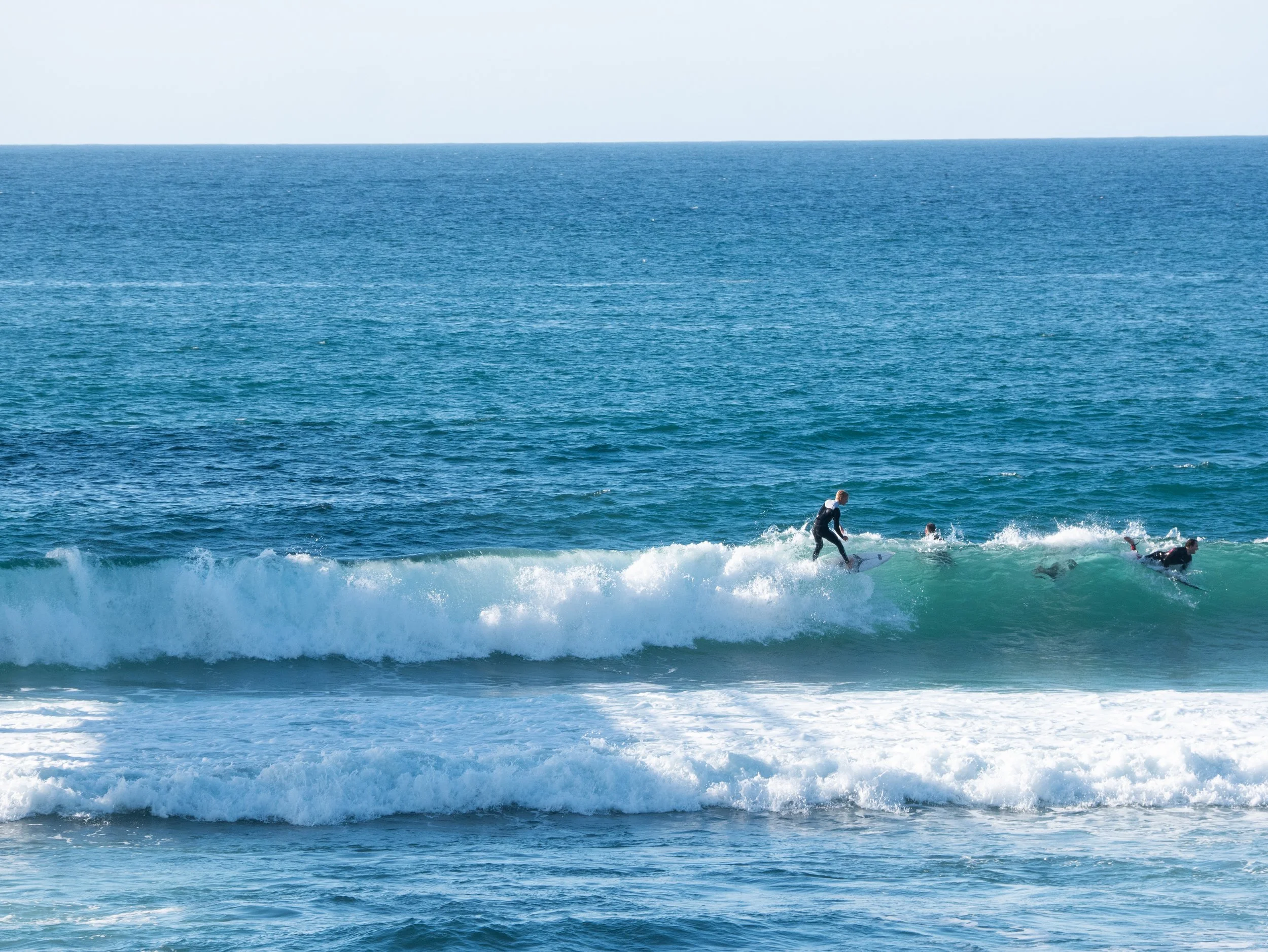 People surfing on ocean waves under a clear sky.