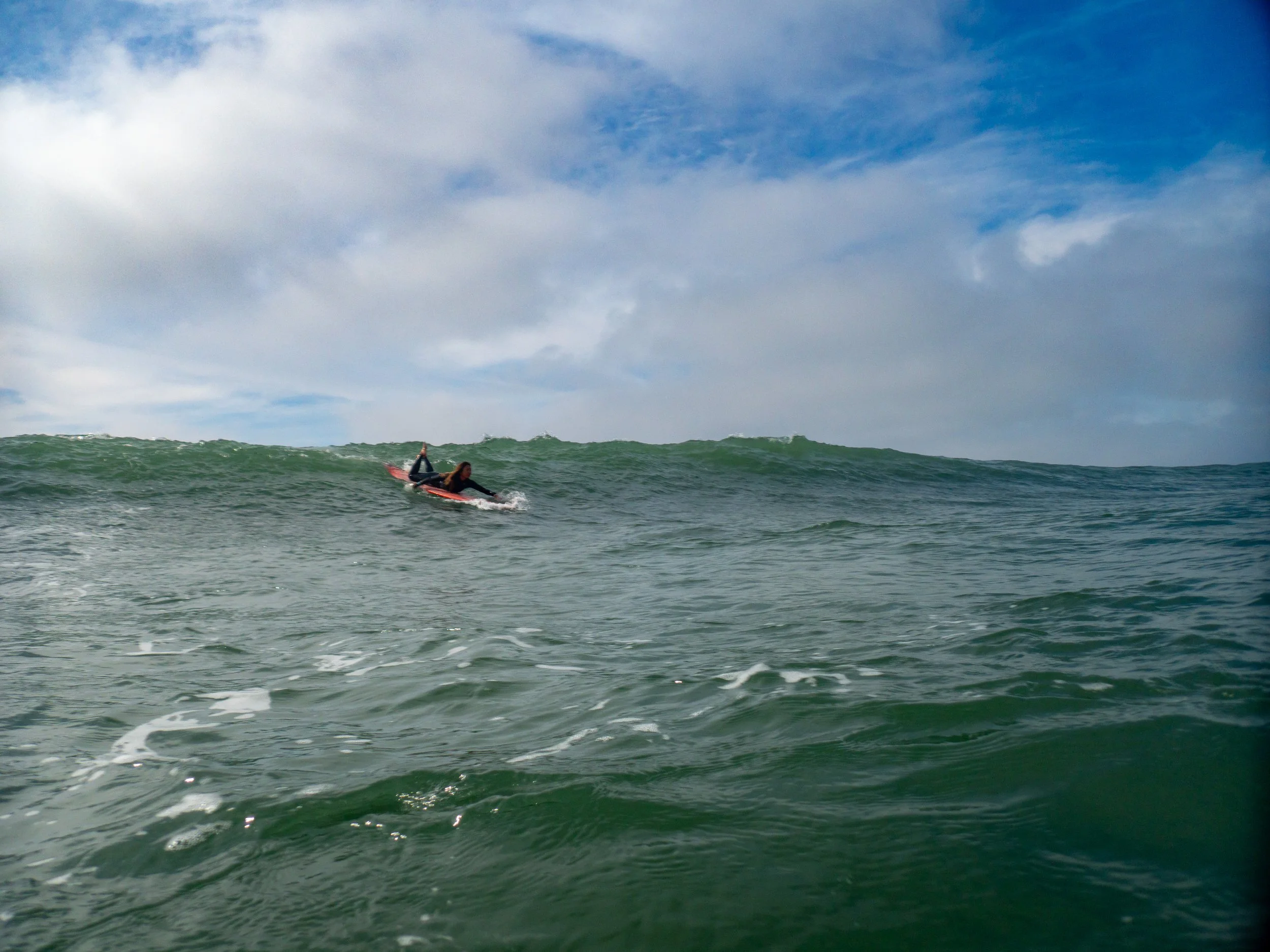 Person surfing on a wave in the ocean under a partly cloudy sky.