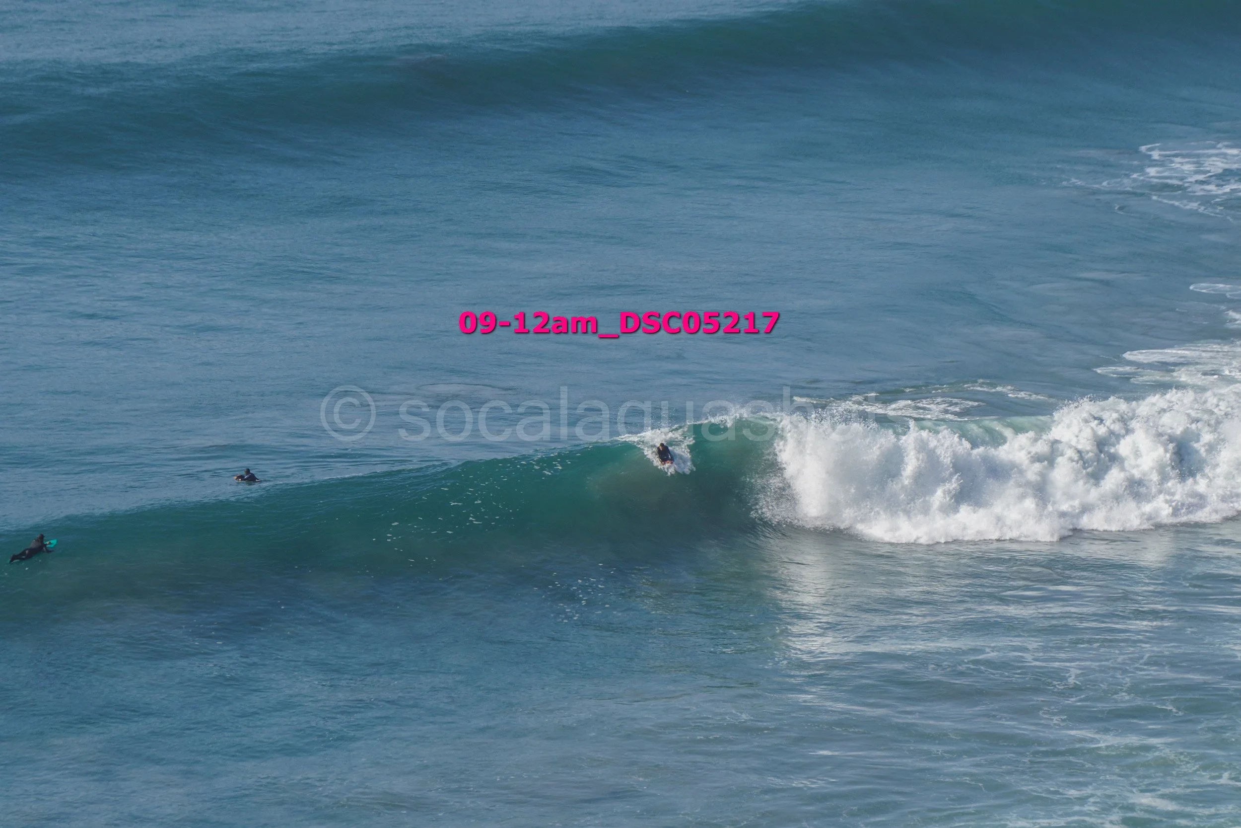 A surfer riding a wave with two other surfers in the water nearby.