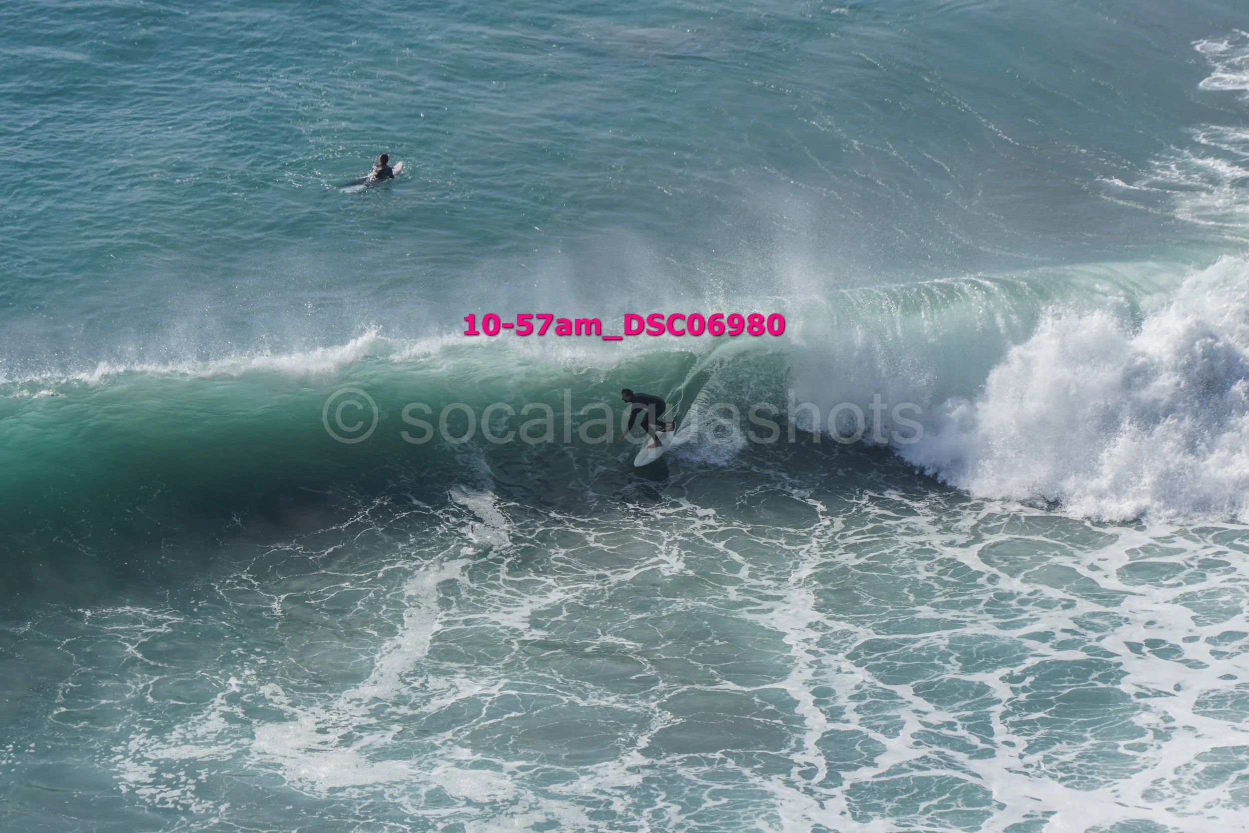 A surfer riding a wave in the ocean with another surfer swimming in the background.