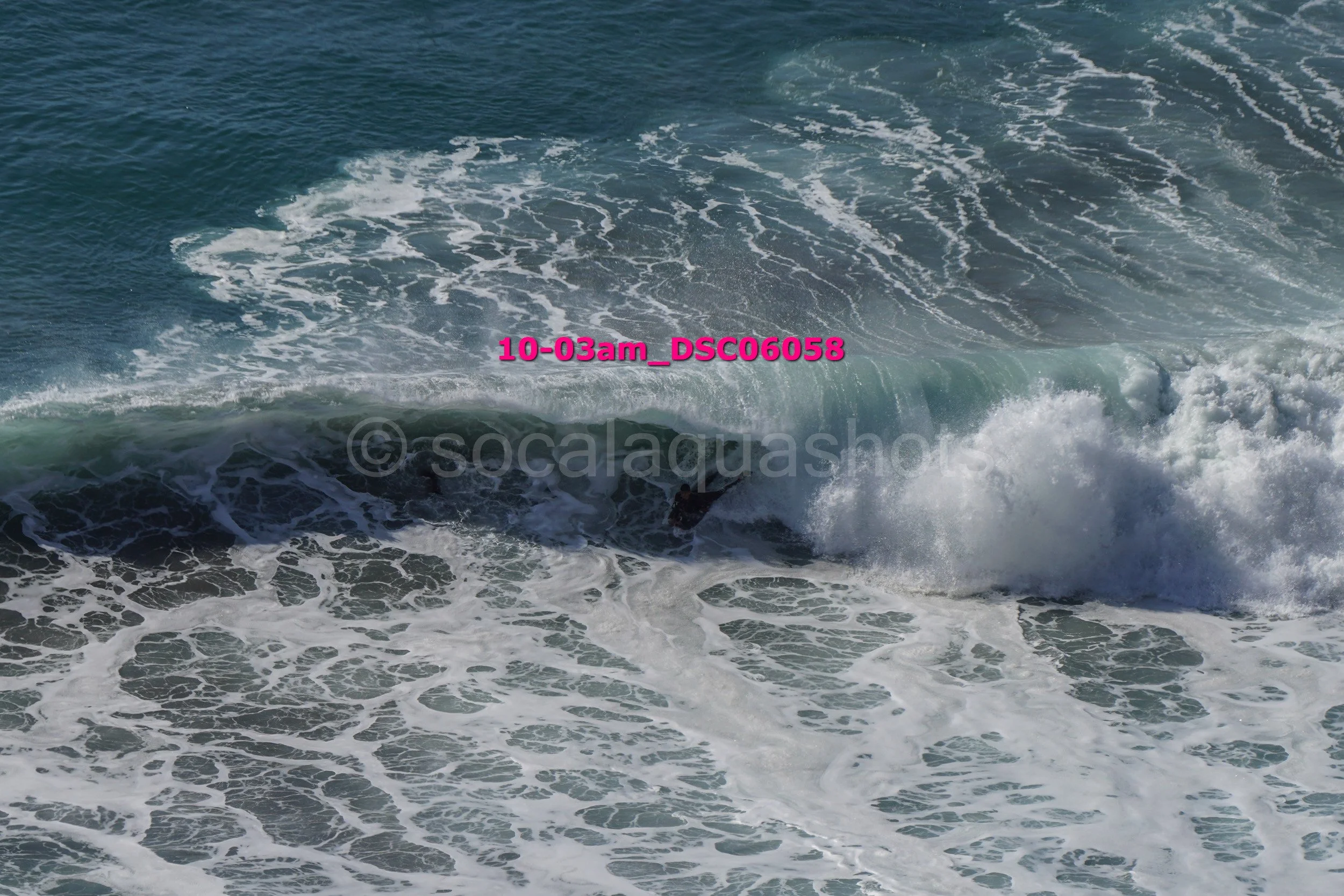 A surfer riding a wave in the ocean, with white foam and blue water.