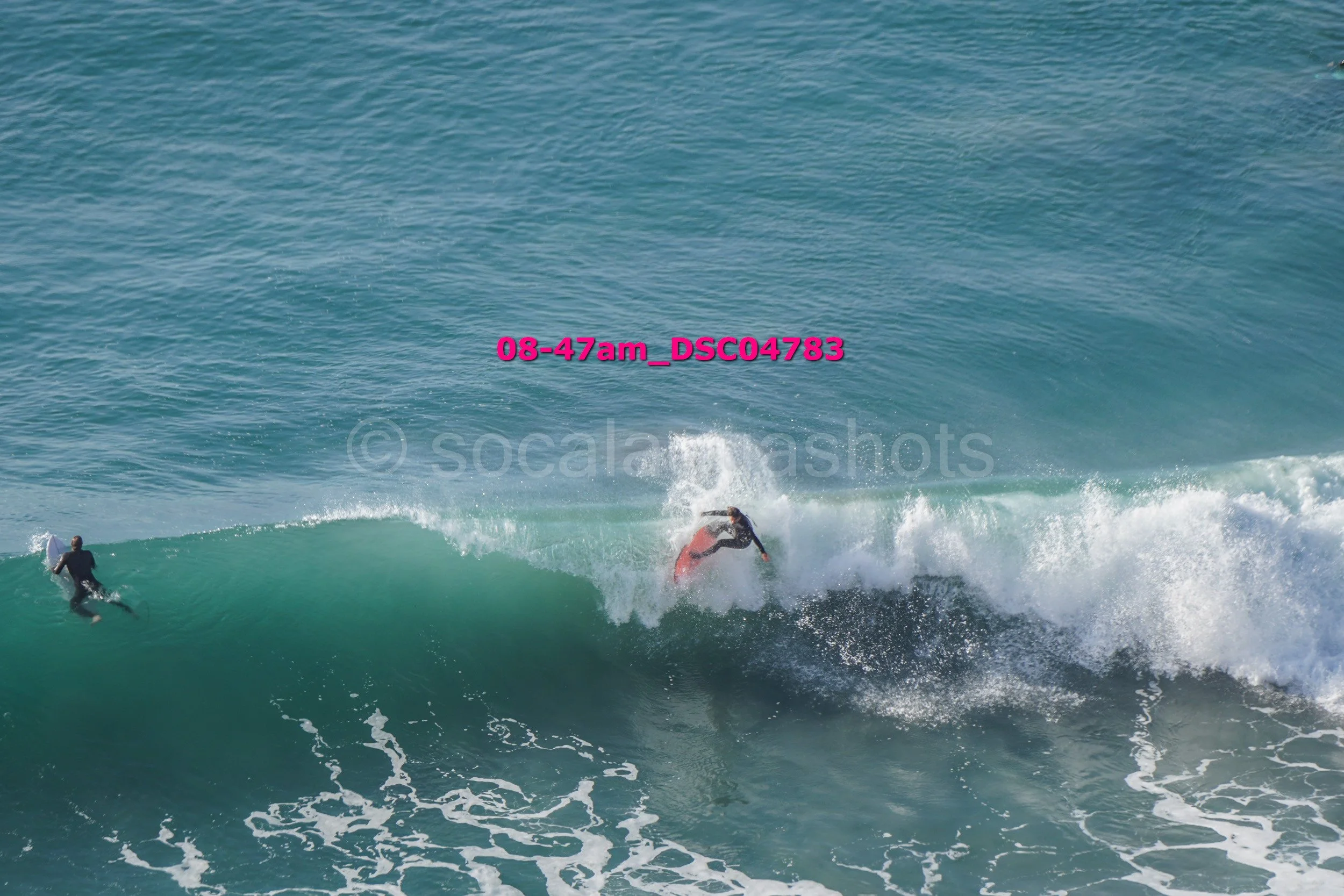 A person surfing on a wave in the ocean, with another person in the water nearby.