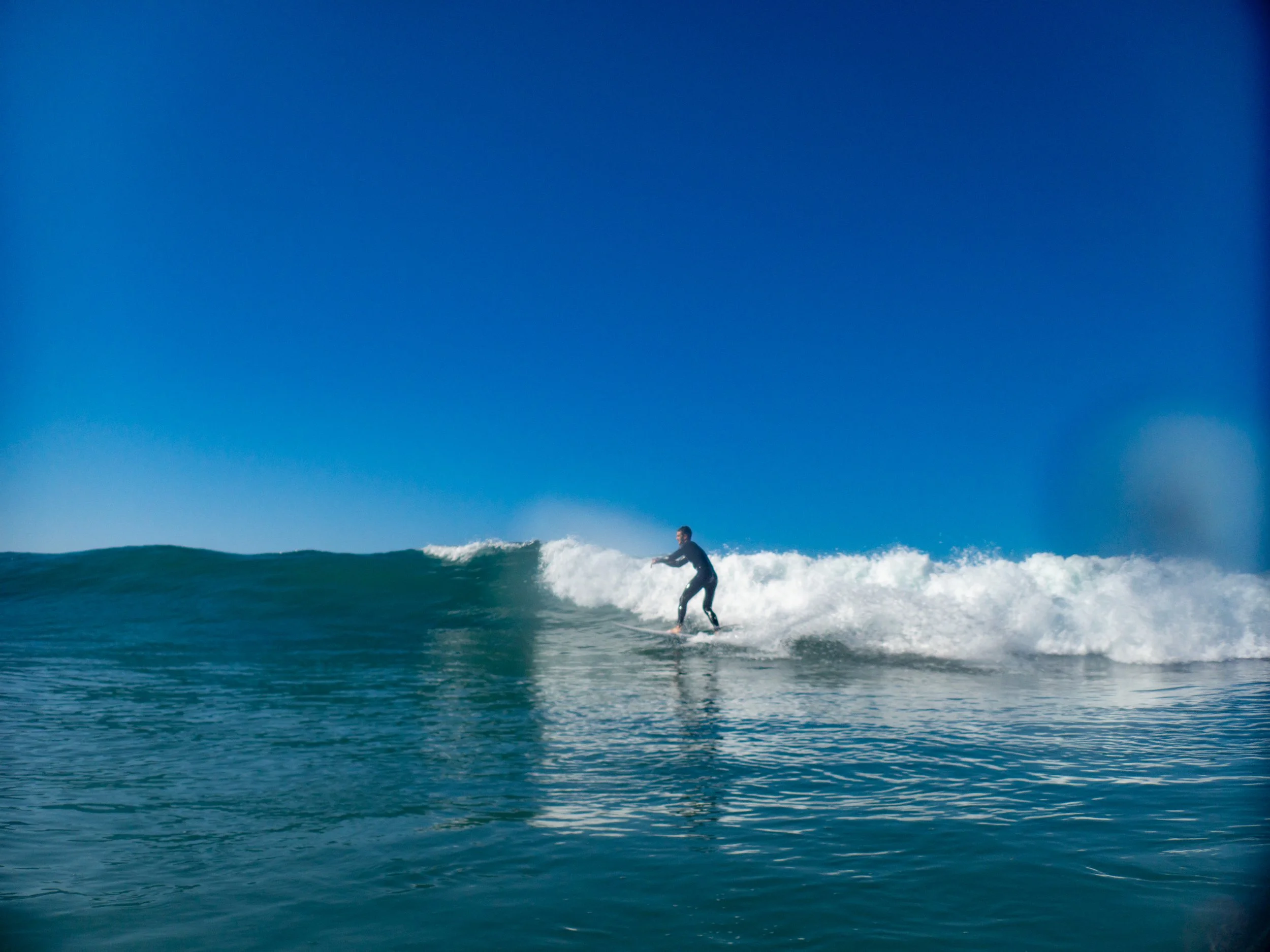 A person surfing on a wave in the ocean under a clear blue sky.
