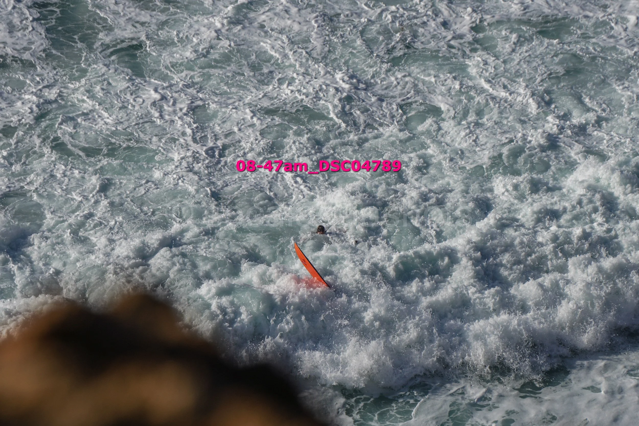 A person with a surfboard in turbulent ocean waves, partially submerged in water with waves crashing around.