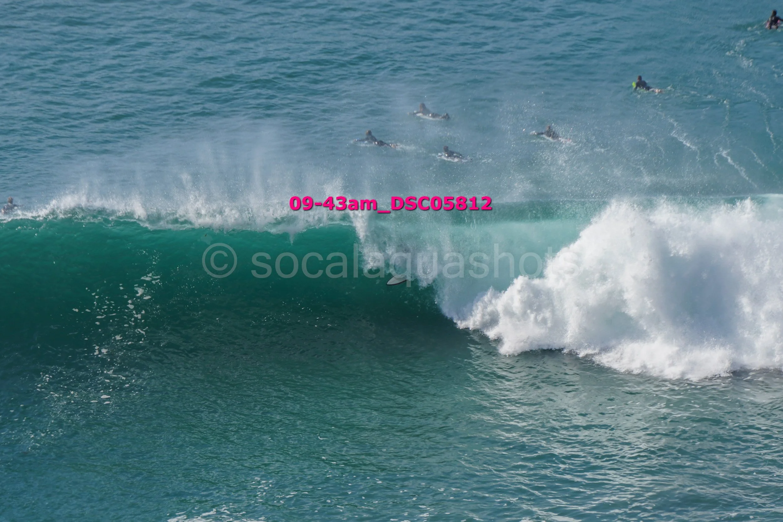 Multiple surfers riding ocean waves, some submerged and others in the water, with one surfer close to the wave's crest.