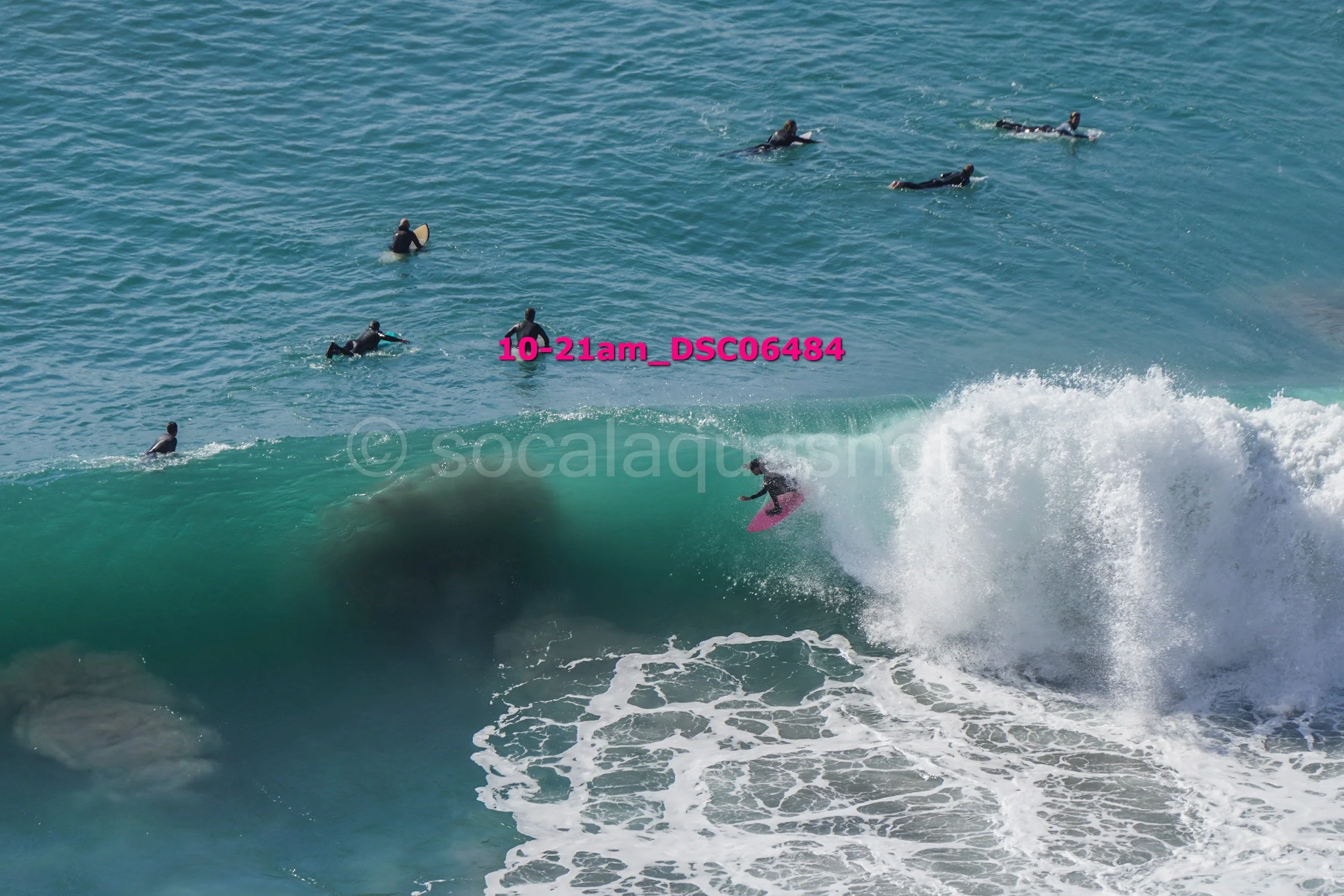 Surfer riding a wave with several people swimming in the ocean nearby.