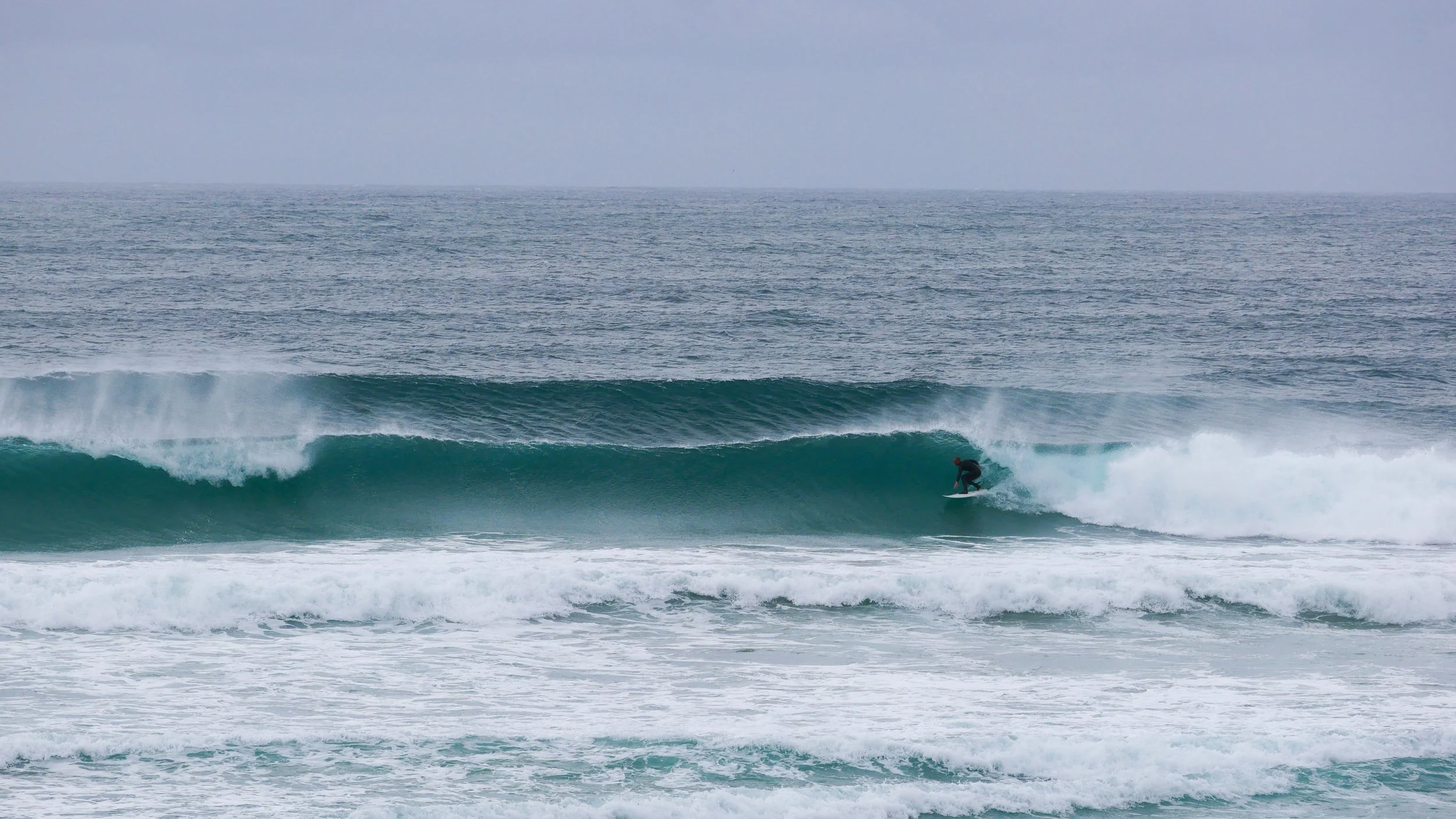 Surfer riding a wave in the ocean under cloudy skies.