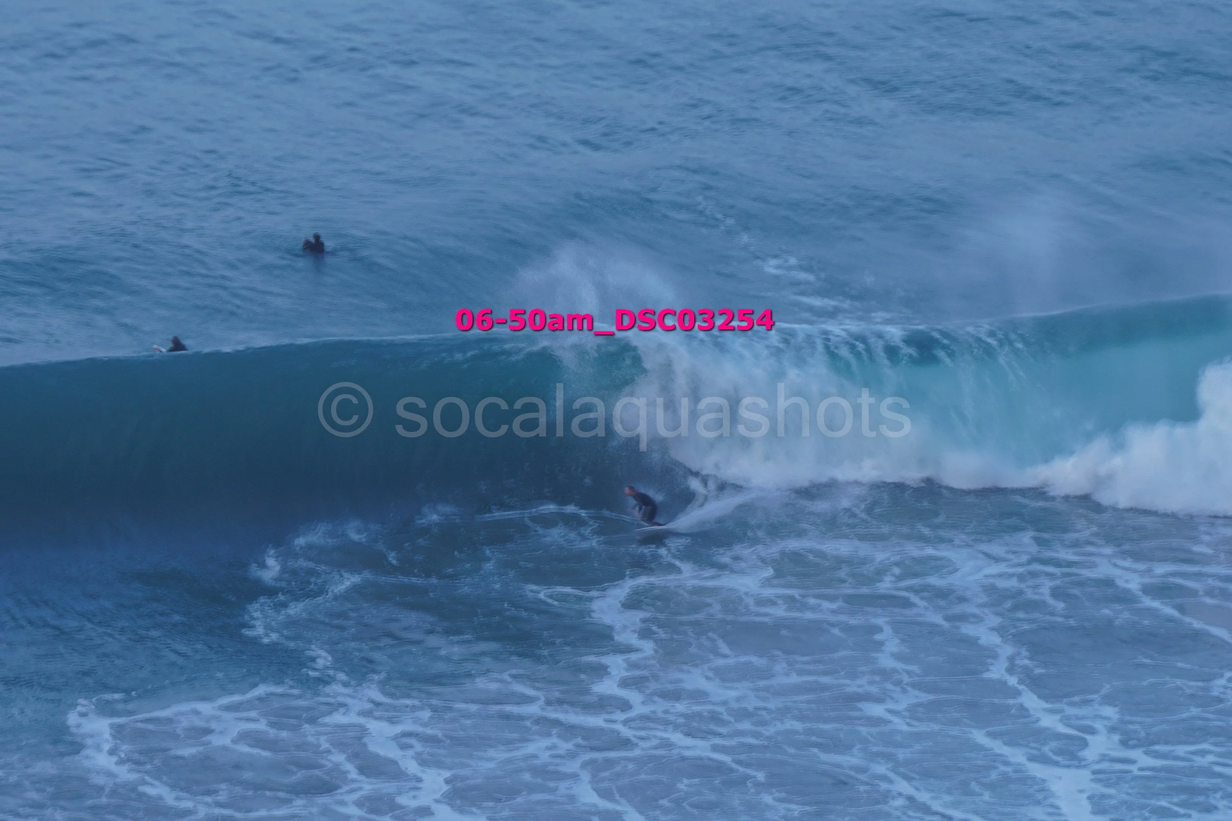 A surfer riding a large wave while two other surfers are in the water nearby in the ocean.