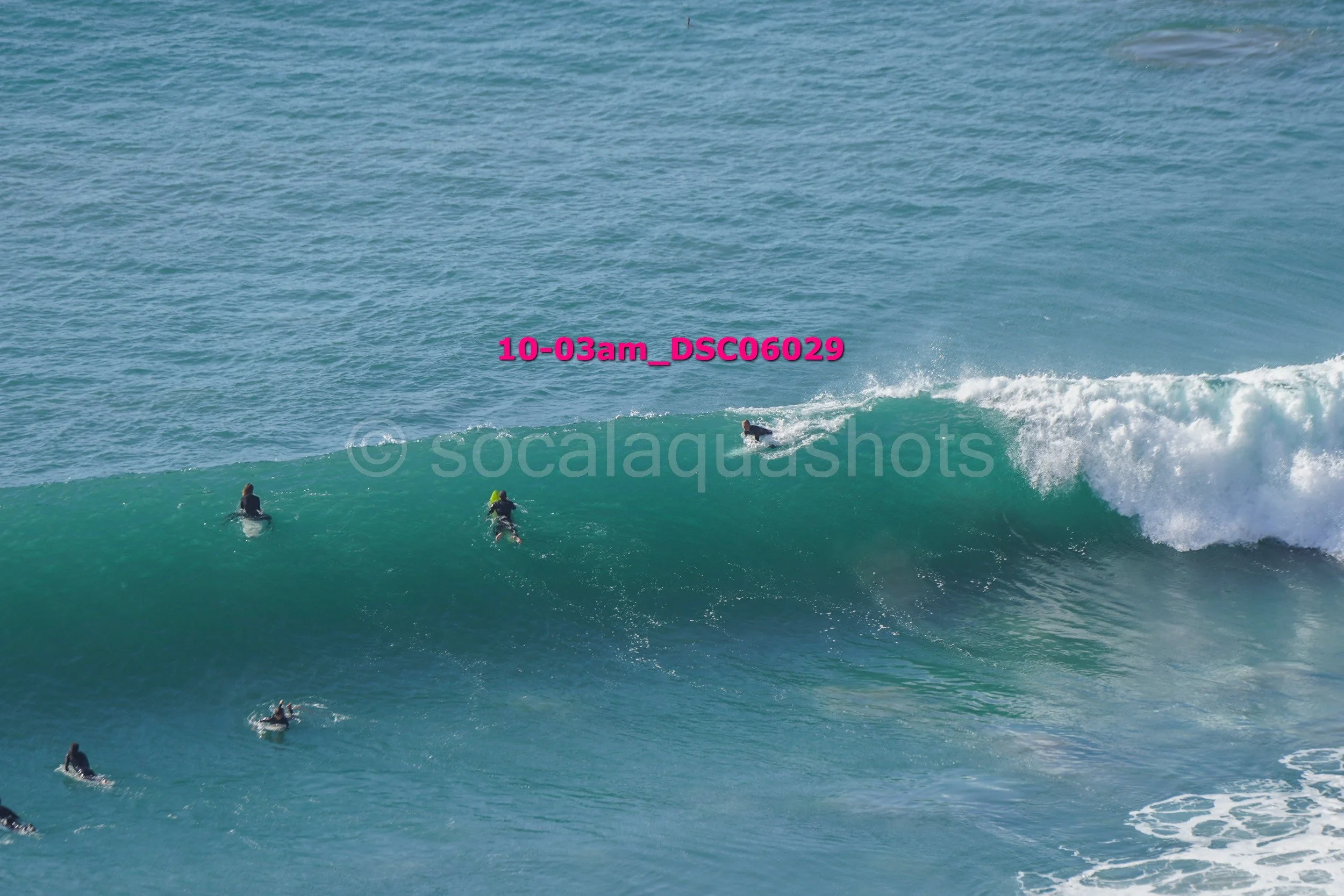 Multiple surfers waiting to ride a large ocean wave.