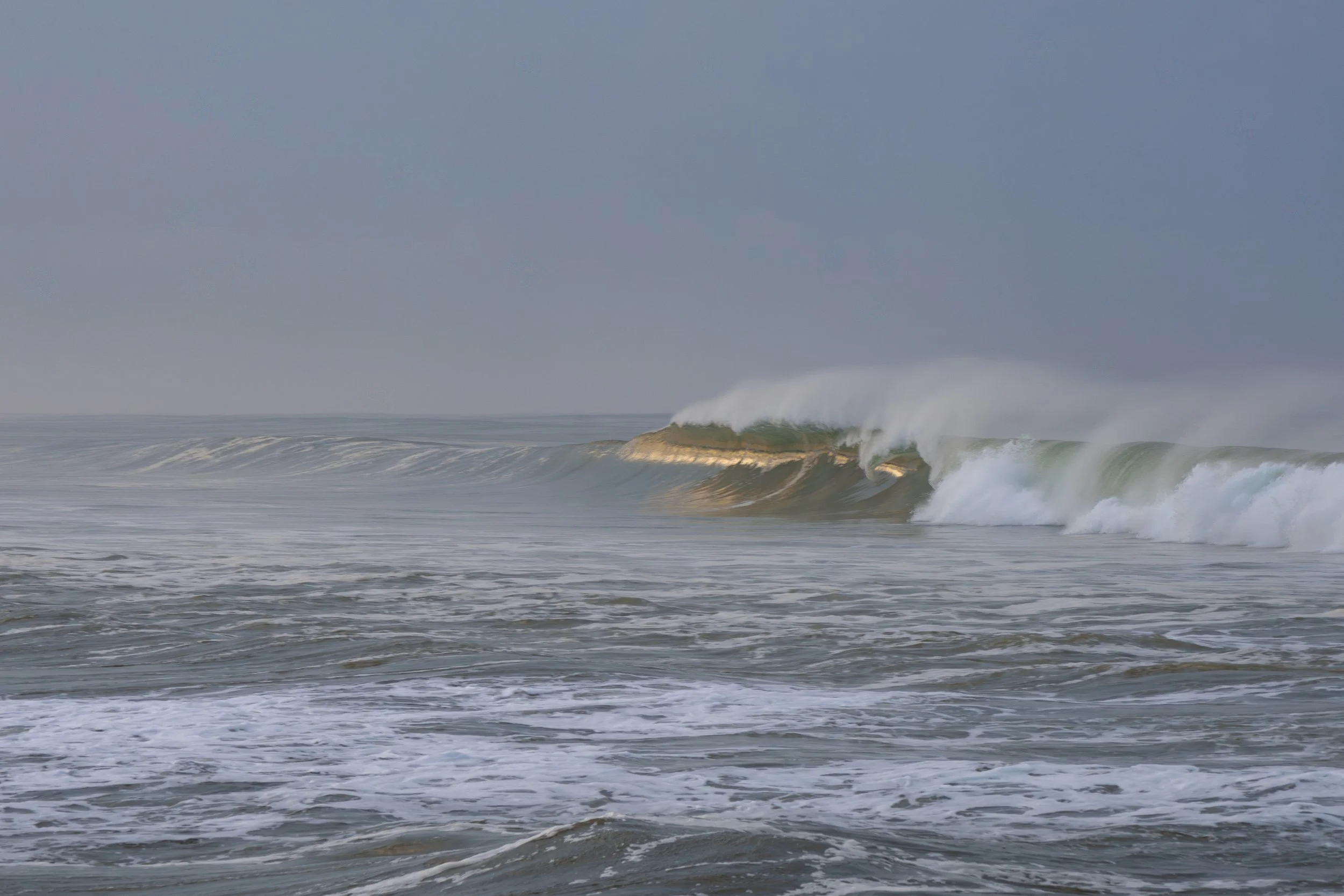 Ocean waves crashing near the shore under a cloudy sky.