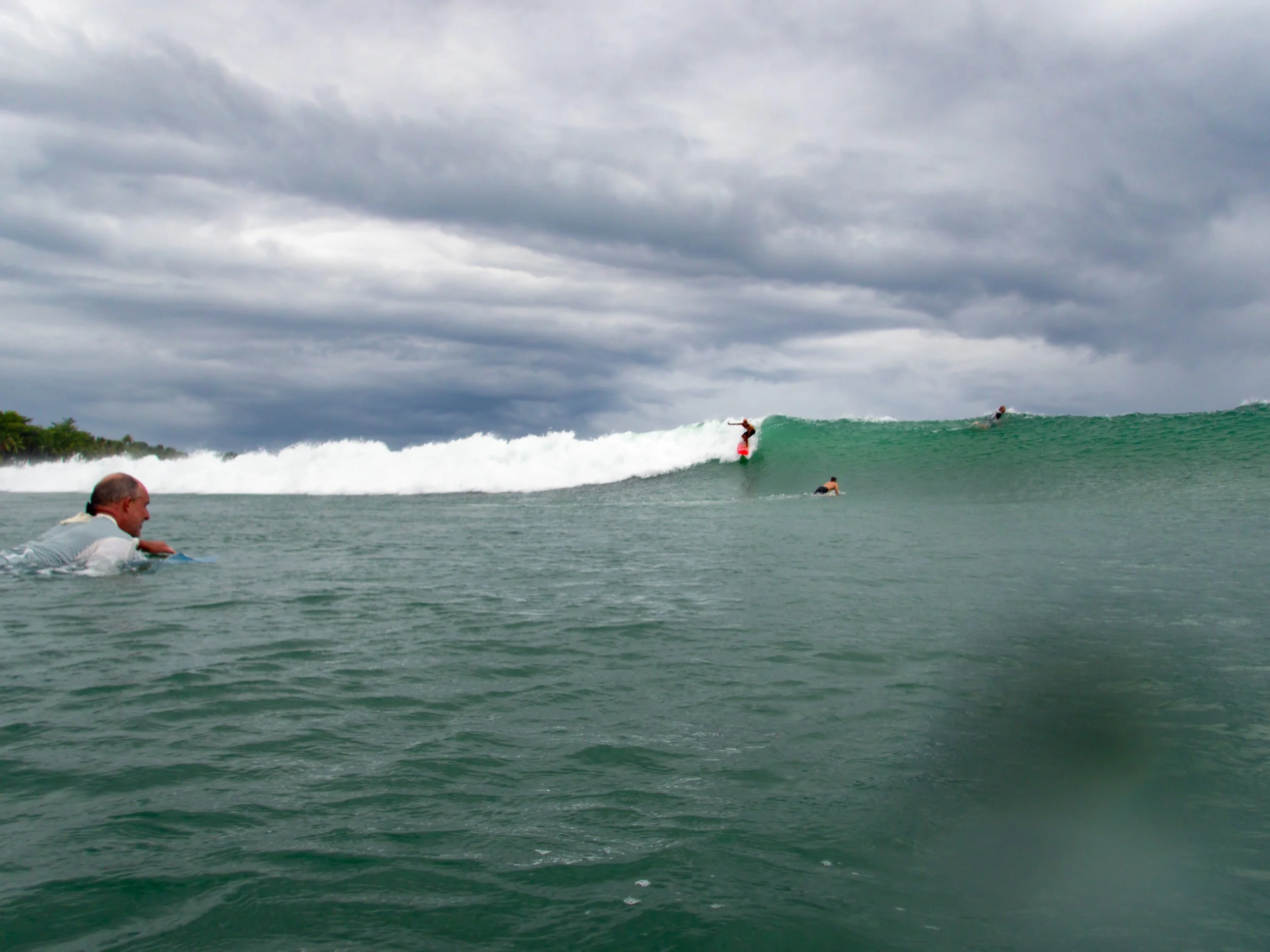 Surfers in ocean paddling and riding waves under cloudy sky