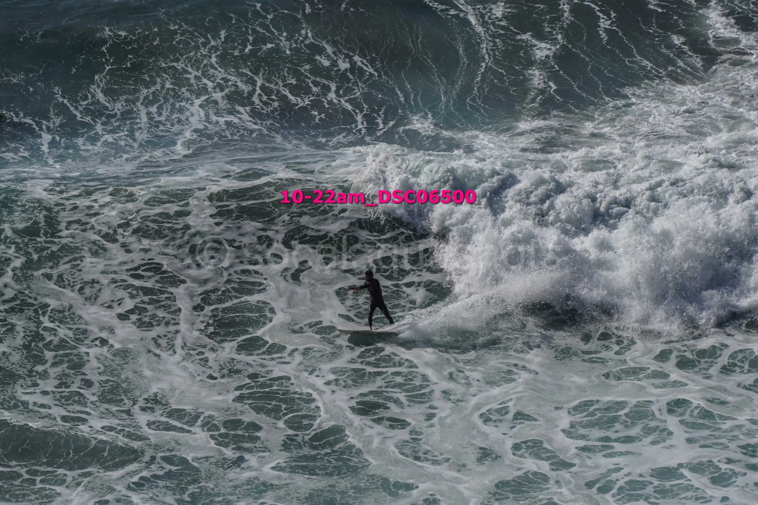 A person surfing on the ocean waves during daylight, surrounded by white foam and churning water.