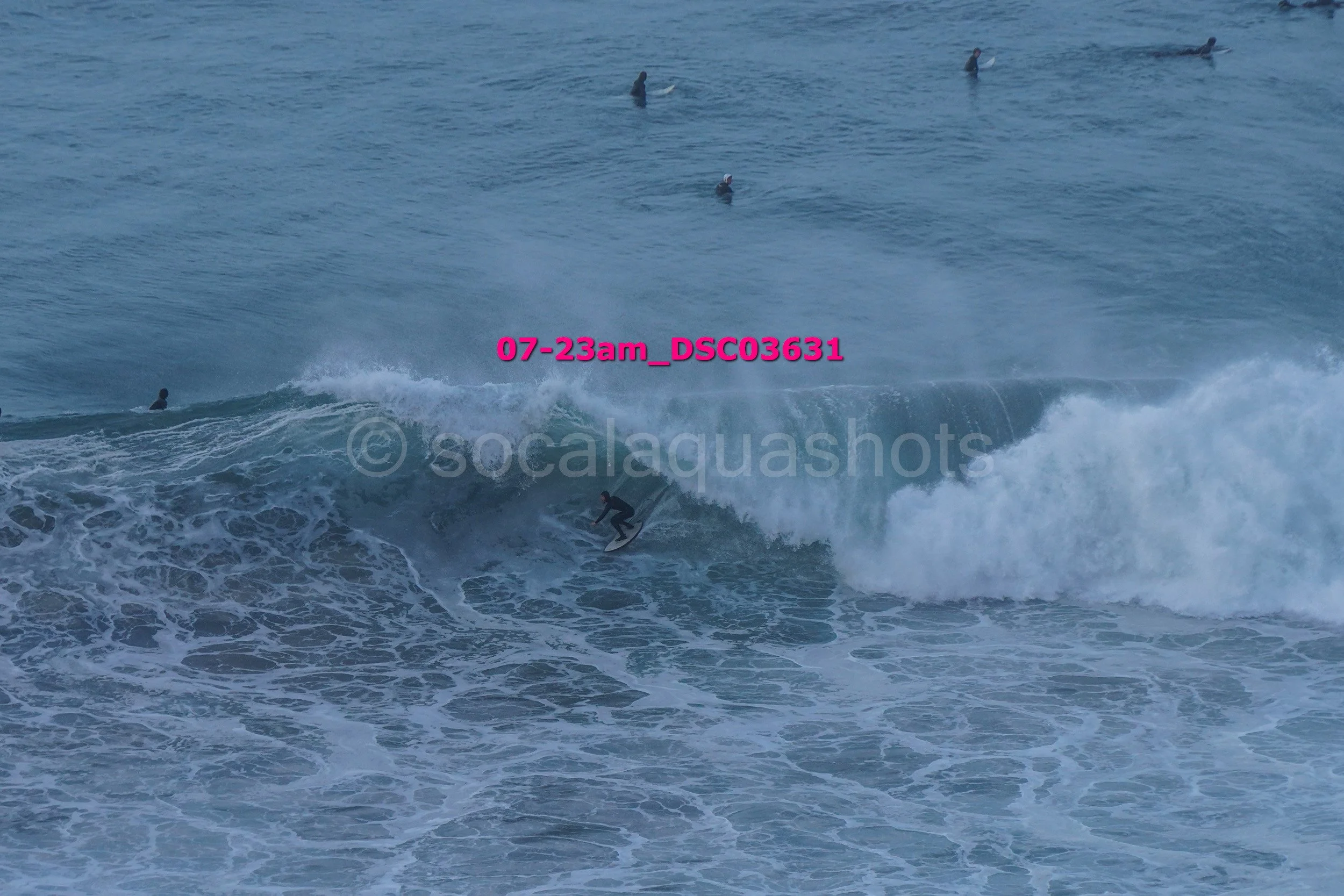 Surfer riding a wave with several people surfing in the background in the ocean.