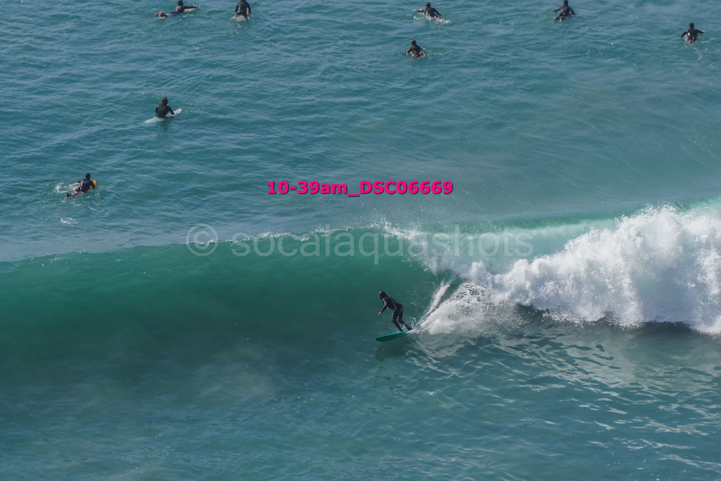 A person surfing on a wave in the ocean with multiple people swimming or surfing in the background.