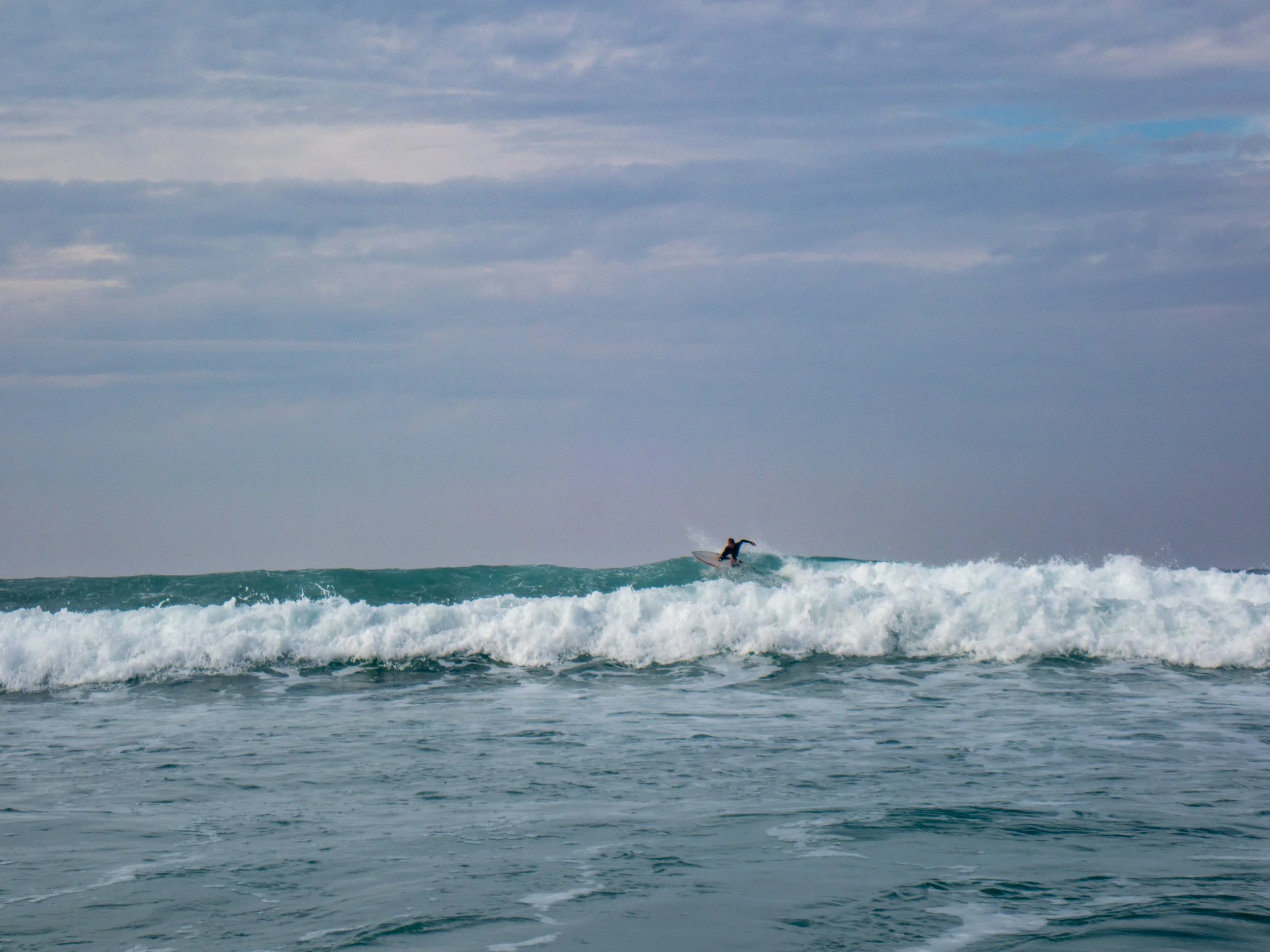 A person surfing on a wave in the ocean with a cloudy sky above.