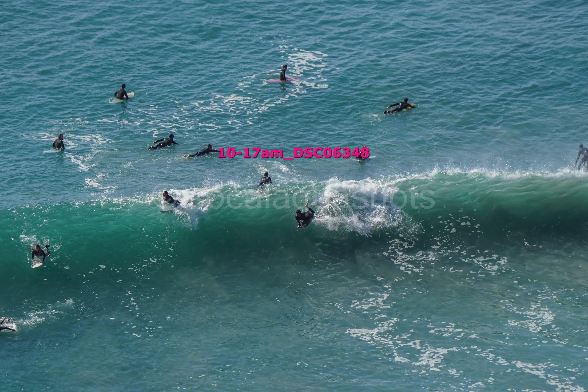 Group of people surfing on ocean waves, some riding waves and others paddling out.