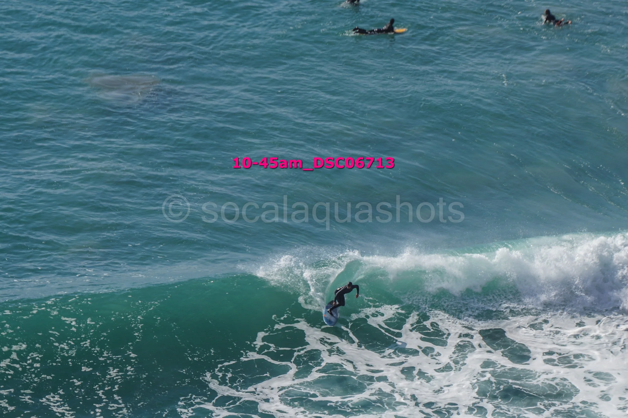 A person surfing on a wave in the ocean with a few other surfers in the background.