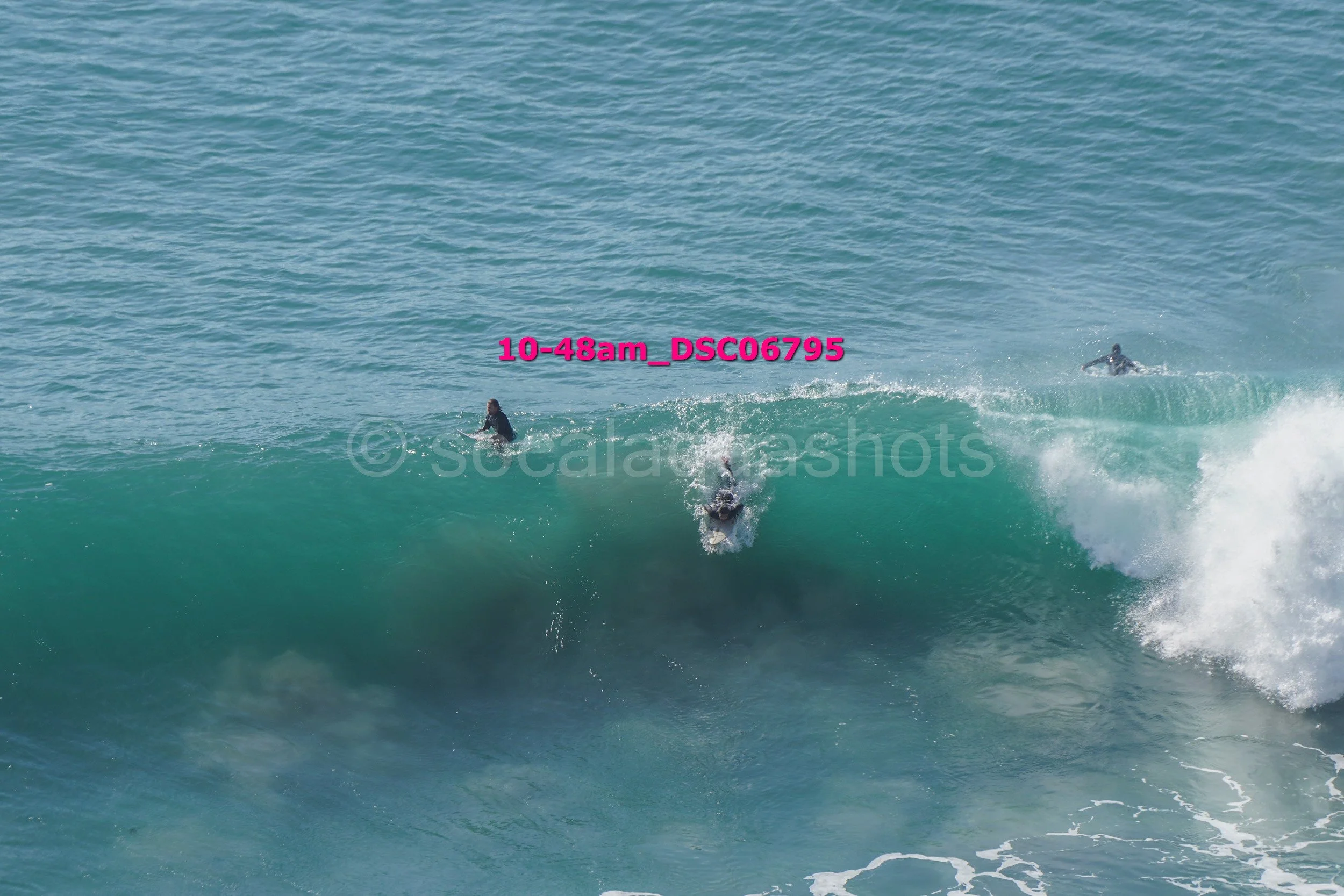 Surfer riding a large wave with two other surfers nearby in the ocean.