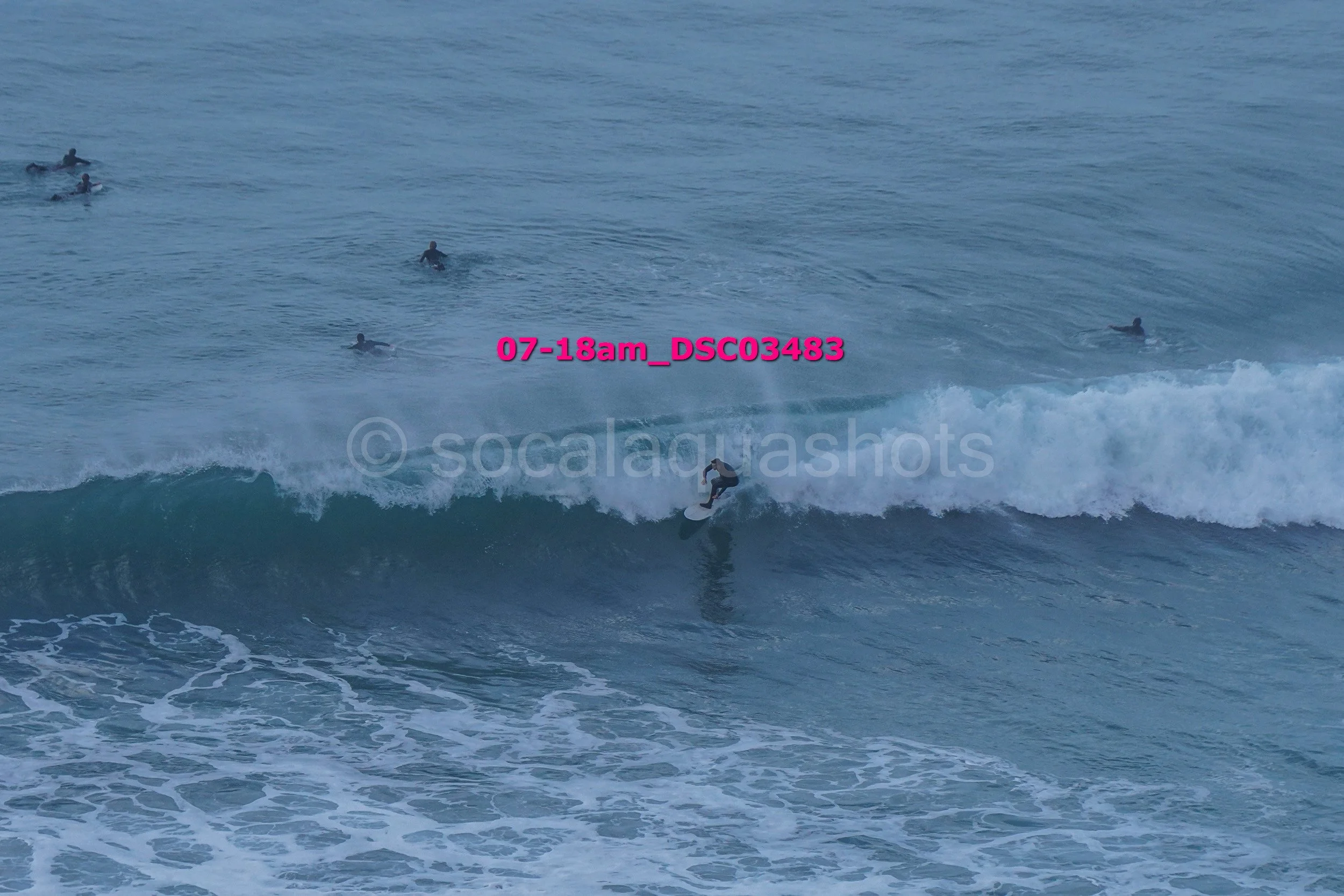 Surfer riding a wave with several people swimming in the background in the ocean.